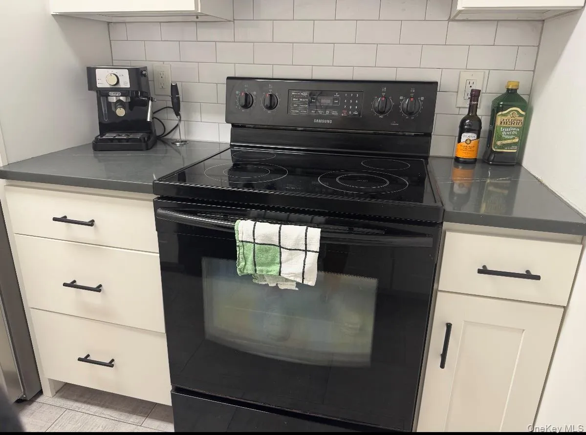 Kitchen featuring black electric range, tasteful backsplash, and white cabinetry Kitchen featuring black electric range, tasteful backsplash, and white cabinetry