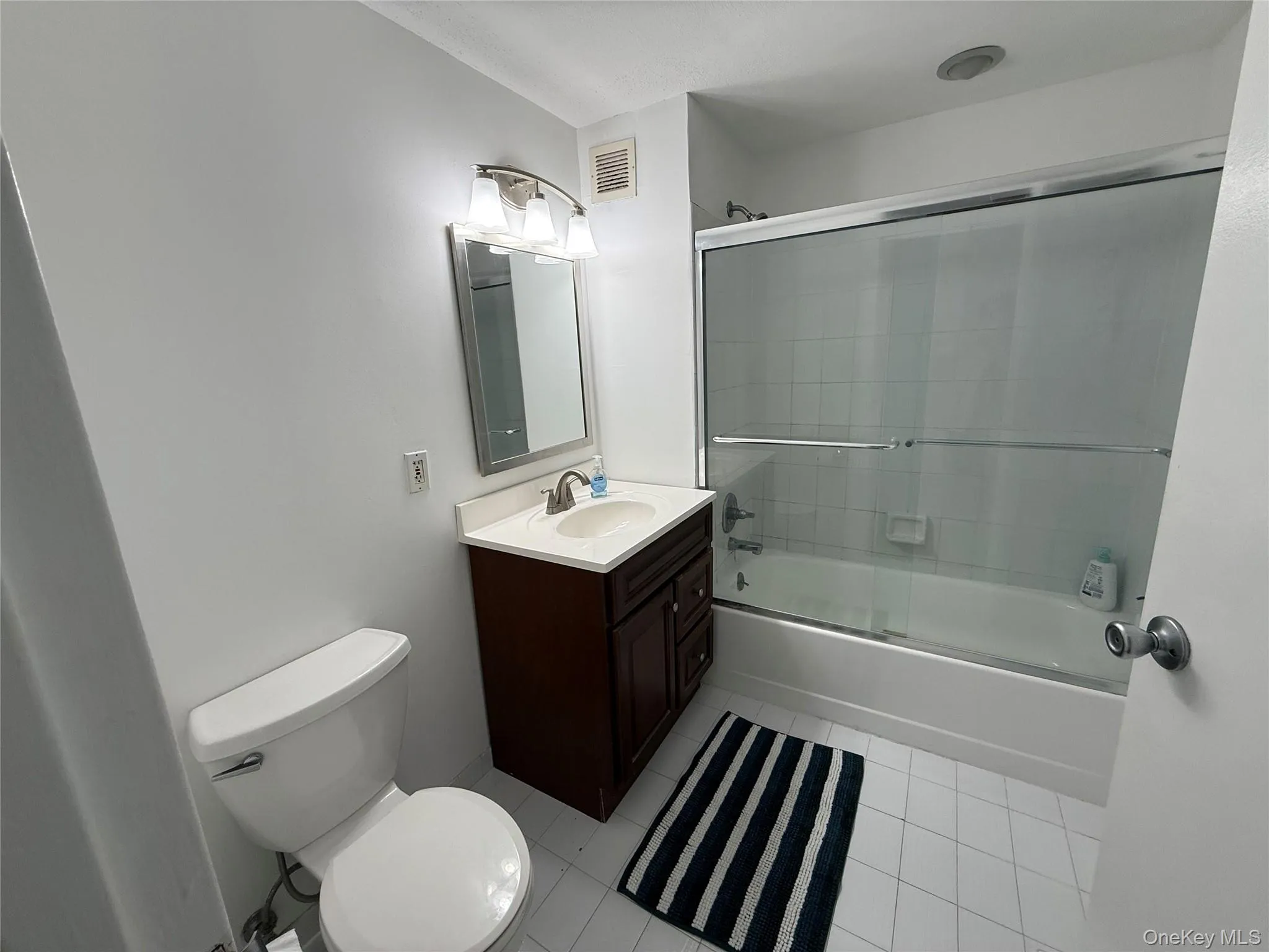 Full bath featuring light tile patterned floors, enclosed tub / shower combo, and vanity Full bath featuring light tile patterned floors, enclosed tub / shower combo, and vanity