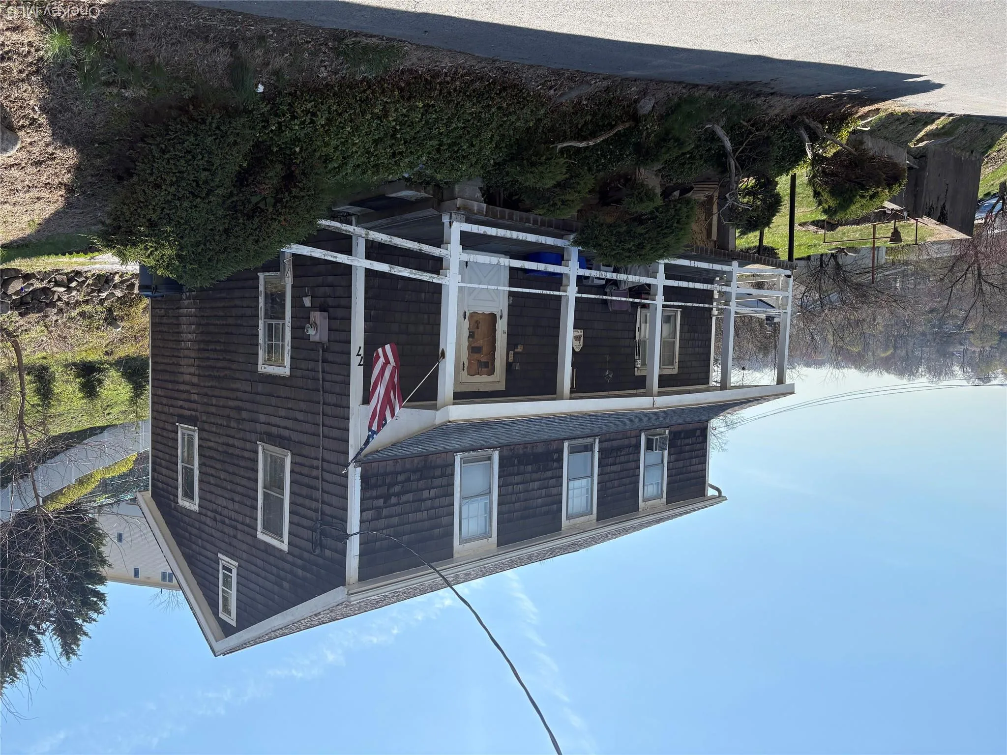 The property features a two-story residence with dark shingle siding and a prominent front porch The property features a two-story residence with dark shingle siding and a prominent front porch