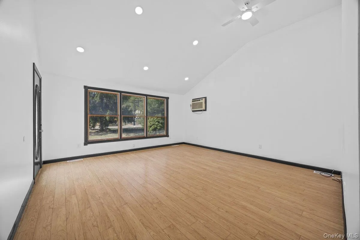 This room features light-toned wood flooring, a window offering views of trees, and a ceiling fan This room features light-toned wood flooring, a window offering views of trees, and a ceiling fan