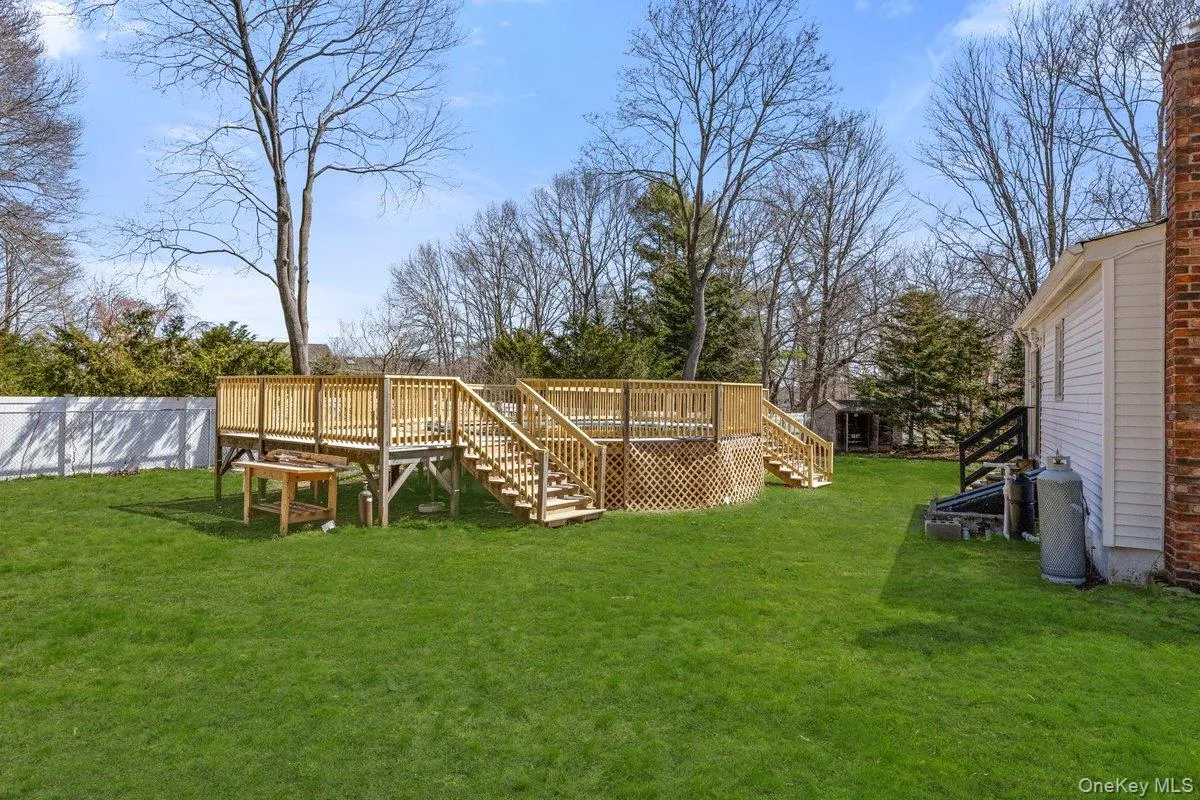 Expansive backyard featuring a well-maintained lawn, a spacious wooden deck with railings, and a white picket fence Expansive backyard featuring a well-maintained lawn, a spacious wooden deck with railings, and a white picket fence