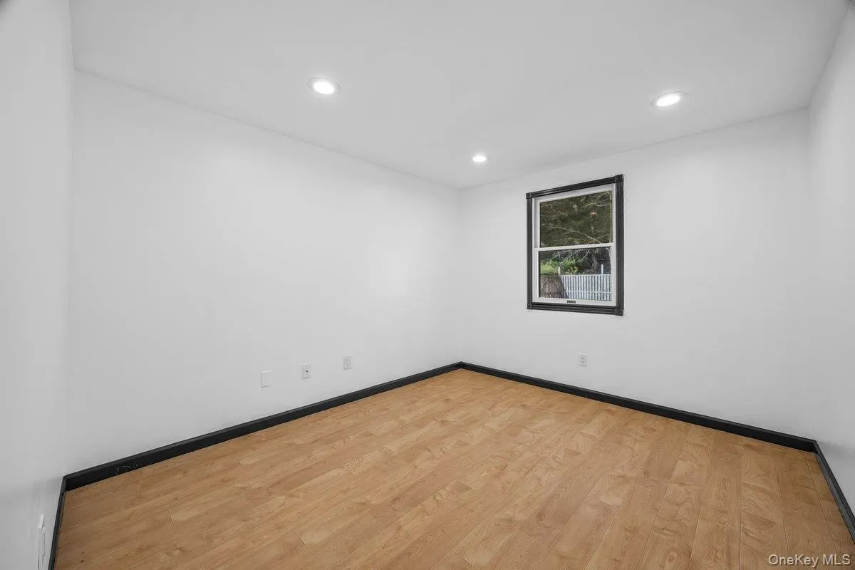 Room with light wood flooring, white walls, and a window with a dark frame Room with light wood flooring, white walls, and a window with a dark frame
