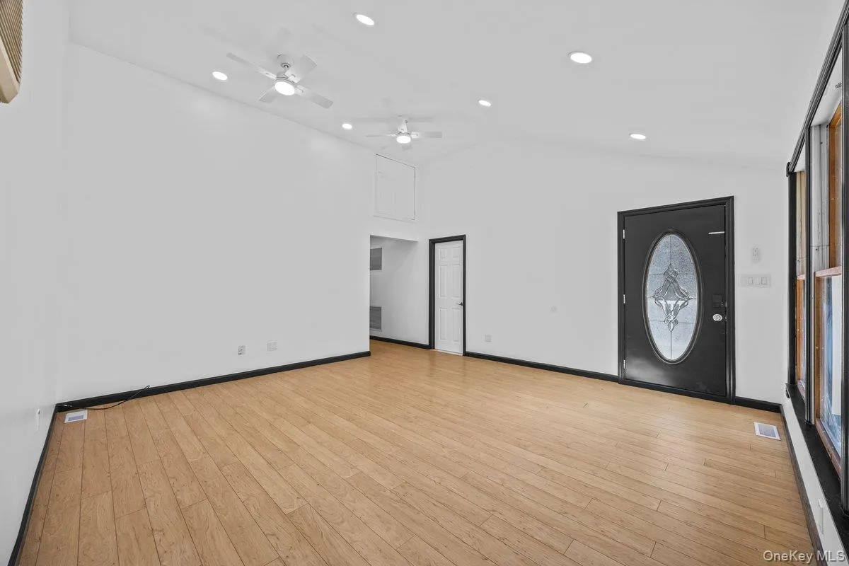 Spacious living area featuring light wood flooring, white walls, and a vaulted ceiling with recessed lighting and ceiling fans Spacious living area featuring light wood flooring, white walls, and a vaulted ceiling with recessed lighting and ceiling fans