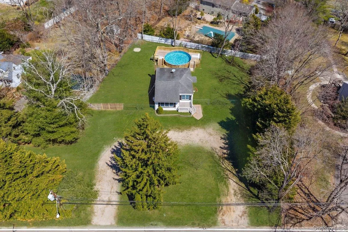 Aerial view of the property featuring a private above-ground pool with a surrounding deck, a well-maintained lawn, and mature trees Aerial view of the property featuring a private above-ground pool with a surrounding deck, a well-maintained lawn, and mature trees