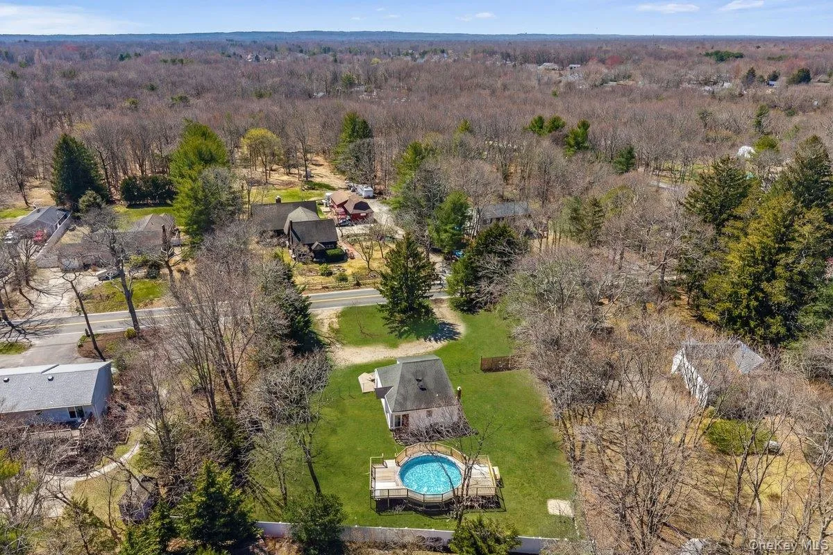 Aerial view showcasing the property with a blue above-ground pool, surrounded by a green lawn and mature trees Aerial view showcasing the property with a blue above-ground pool, surrounded by a green lawn and mature trees