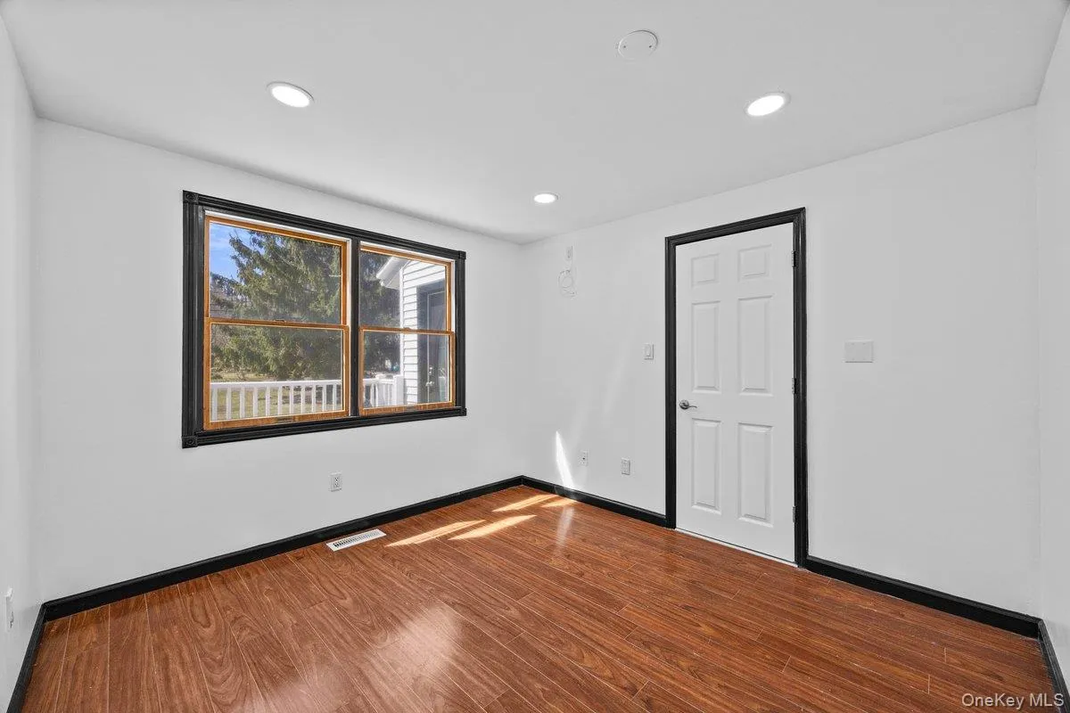 Room featuring hardwood flooring, recessed lighting, and a window with exterior views Room featuring hardwood flooring, recessed lighting, and a window with exterior views