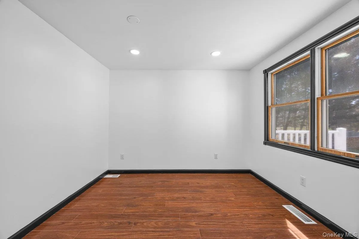 This room features hardwood flooring, white walls, recessed lighting, and windows with dark trim, offering natural light This room features hardwood flooring, white walls, recessed lighting, and windows with dark trim, offering natural light