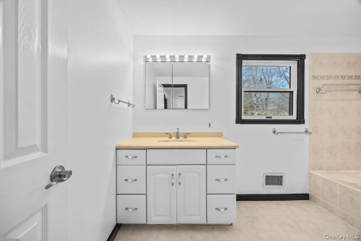 The bathroom features a vanity with a countertop, a sink, and cabinet storage, complemented by a lighted mirror The bathroom features a vanity with a countertop, a sink, and cabinet storage, complemented by a lighted mirror