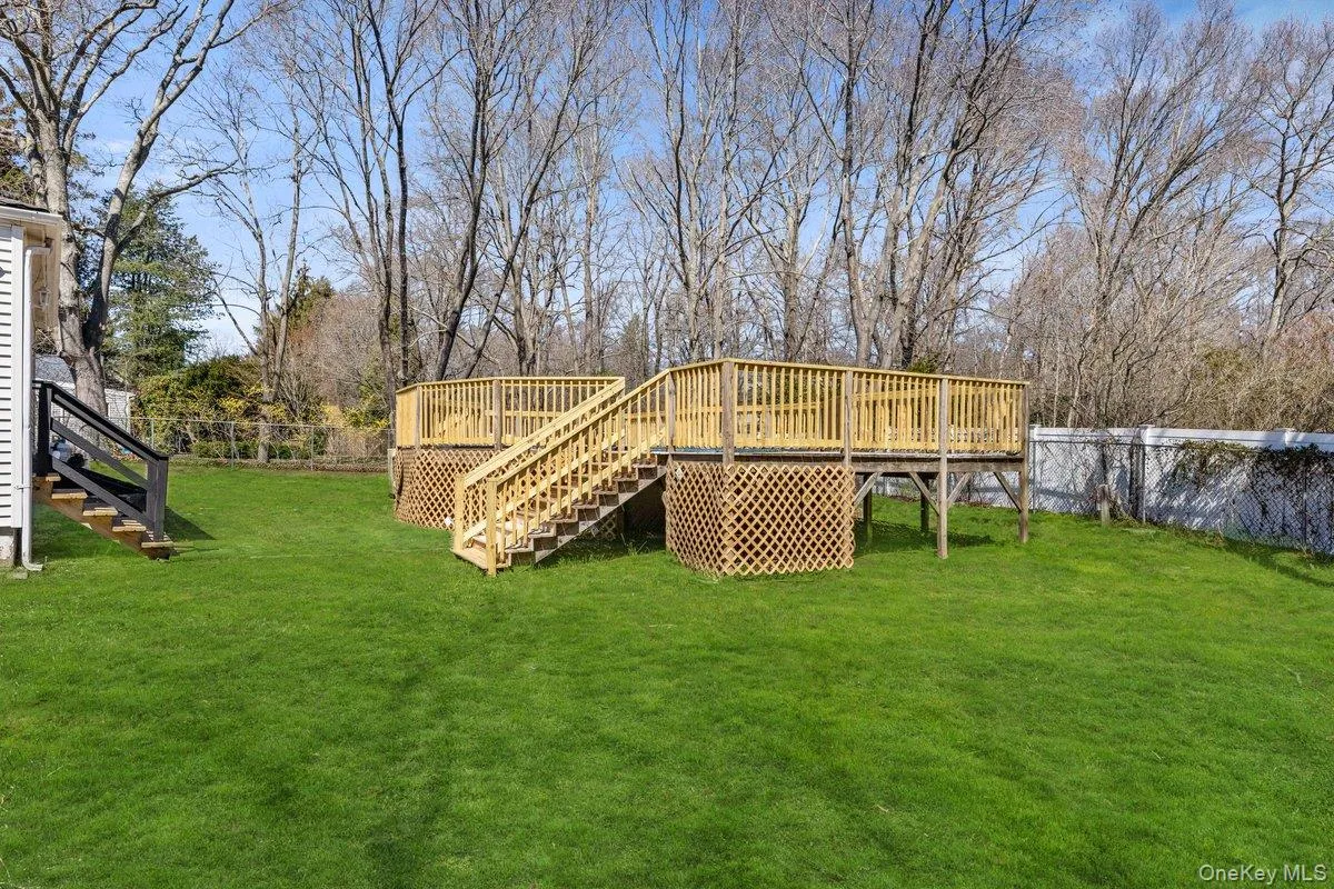 The property features a spacious yard with a large lawn and a wooden deck, complete with stairs and railings The property features a spacious yard with a large lawn and a wooden deck, complete with stairs and railings