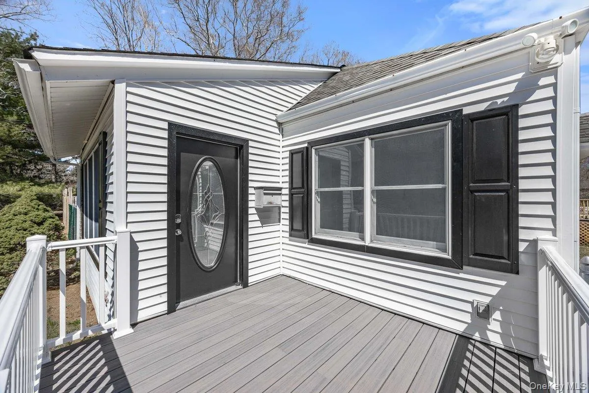 The property features white horizontal siding, a gray deck, and a black oval-lite front door The property features white horizontal siding, a gray deck, and a black oval-lite front door