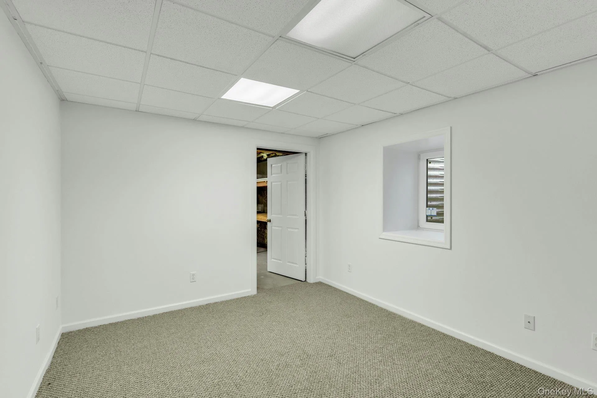 Carpeted room featuring crisp white walls, a drop ceiling with integrated lighting, a white painted door frame, and a window with horizontal blinds Carpeted room featuring crisp white walls, a drop ceiling with integrated lighting, a white painted door frame, and a window with horizontal blinds