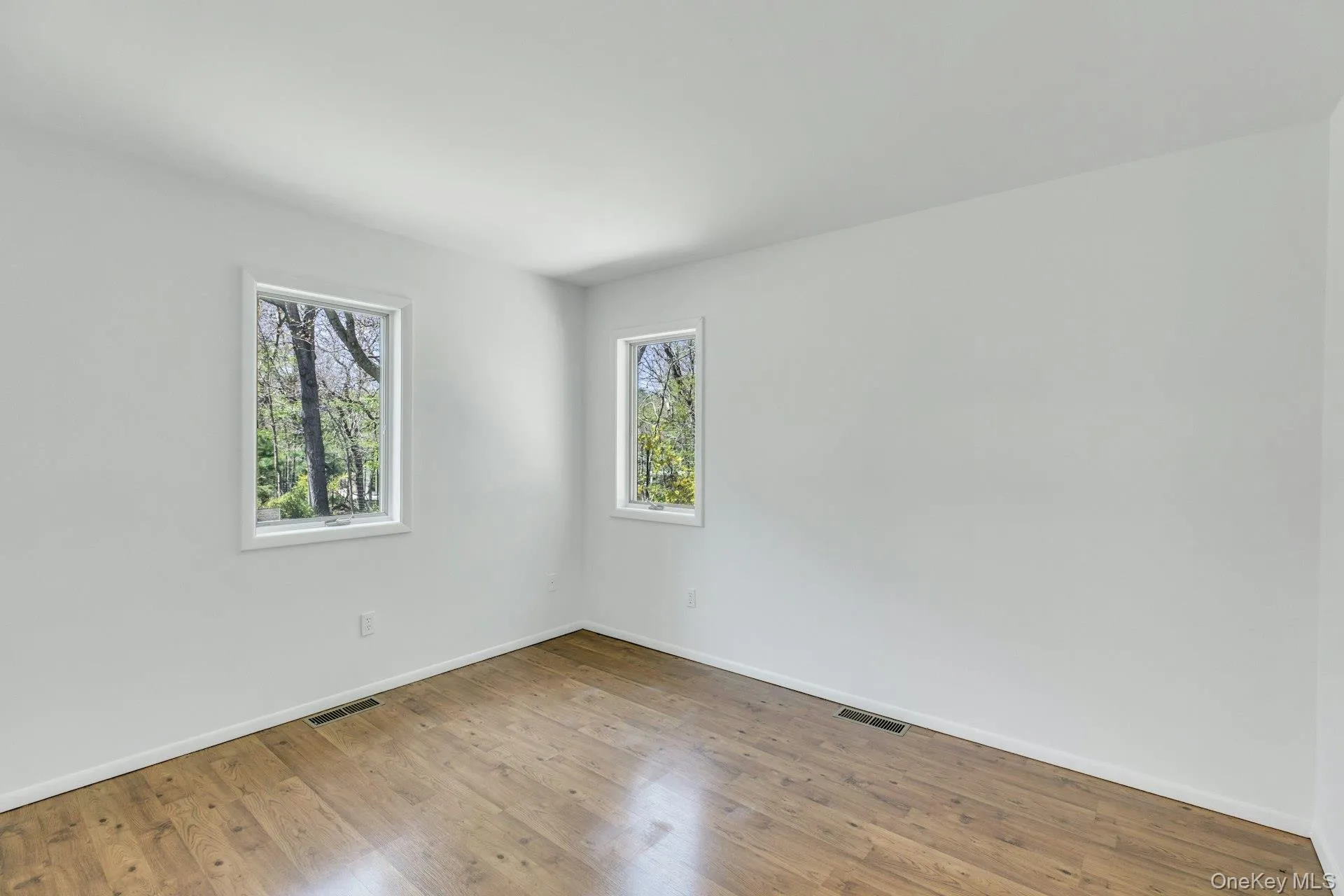 Room featuring wood-finish flooring, white baseboards, and two windows with white trim Room featuring wood-finish flooring, white baseboards, and two windows with white trim
