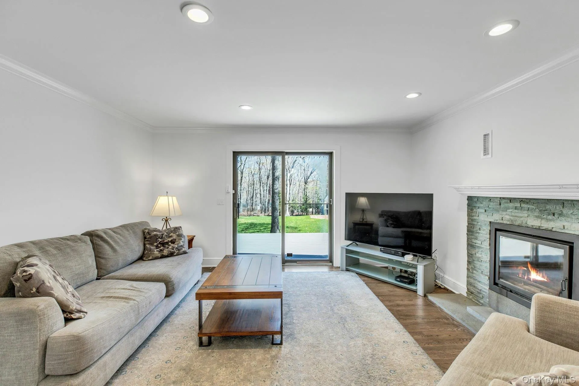 Living space featuring wood-finish flooring, a stacked stone fireplace with a white mantel, and recessed lighting Living space featuring wood-finish flooring, a stacked stone fireplace with a white mantel, and recessed lighting