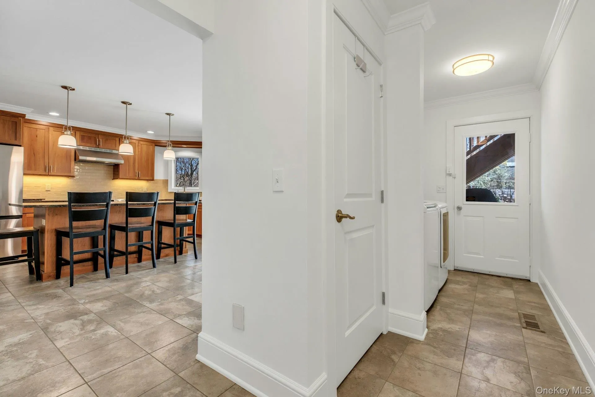 Bright hallway with tile flooring, crown molding, and a white paneled door Bright hallway with tile flooring, crown molding, and a white paneled door