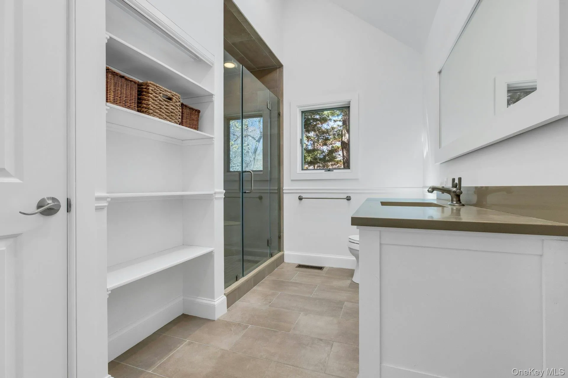 Ensuite Bathroom featuring a frameless glass shower enclosure, a single vanity with a solid surface countertop, an undermount sink, and a wall-mounted mirror Ensuite Bathroom featuring a frameless glass shower enclosure, a single vanity with a solid surface countertop, an undermount sink, and a wall-mounted mirror