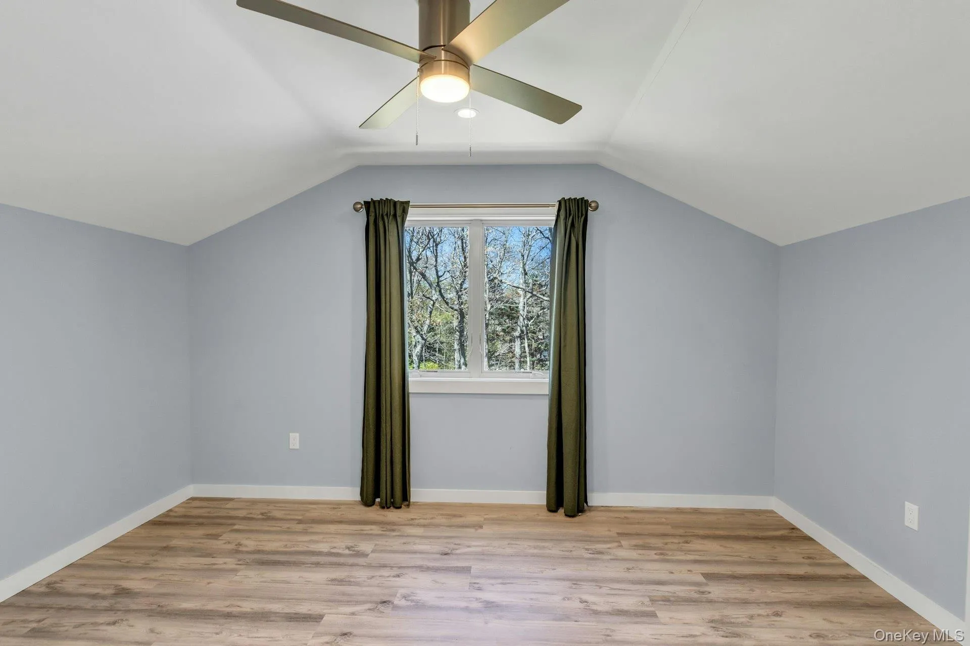 Room featuring sloped ceilings, light blue walls, and wood-finish flooring Room featuring sloped ceilings, light blue walls, and wood-finish flooring