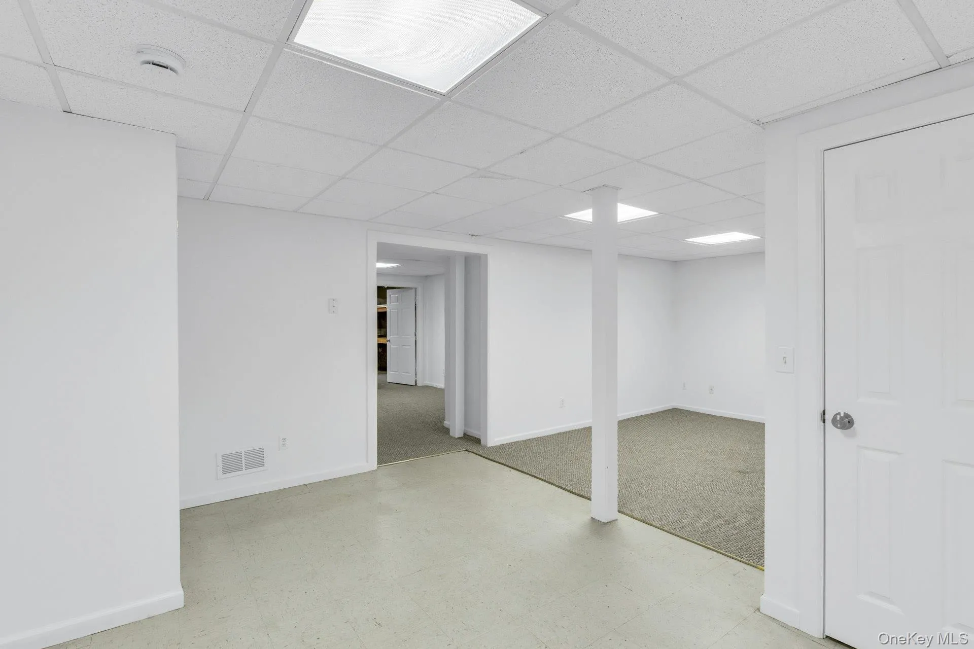 Partially Finished lower level featuring a drop ceiling with recessed lighting, painted support column, white panel door, and light-toned flooring Partially Finished lower level featuring a drop ceiling with recessed lighting, painted support column, white panel door, and light-toned flooring