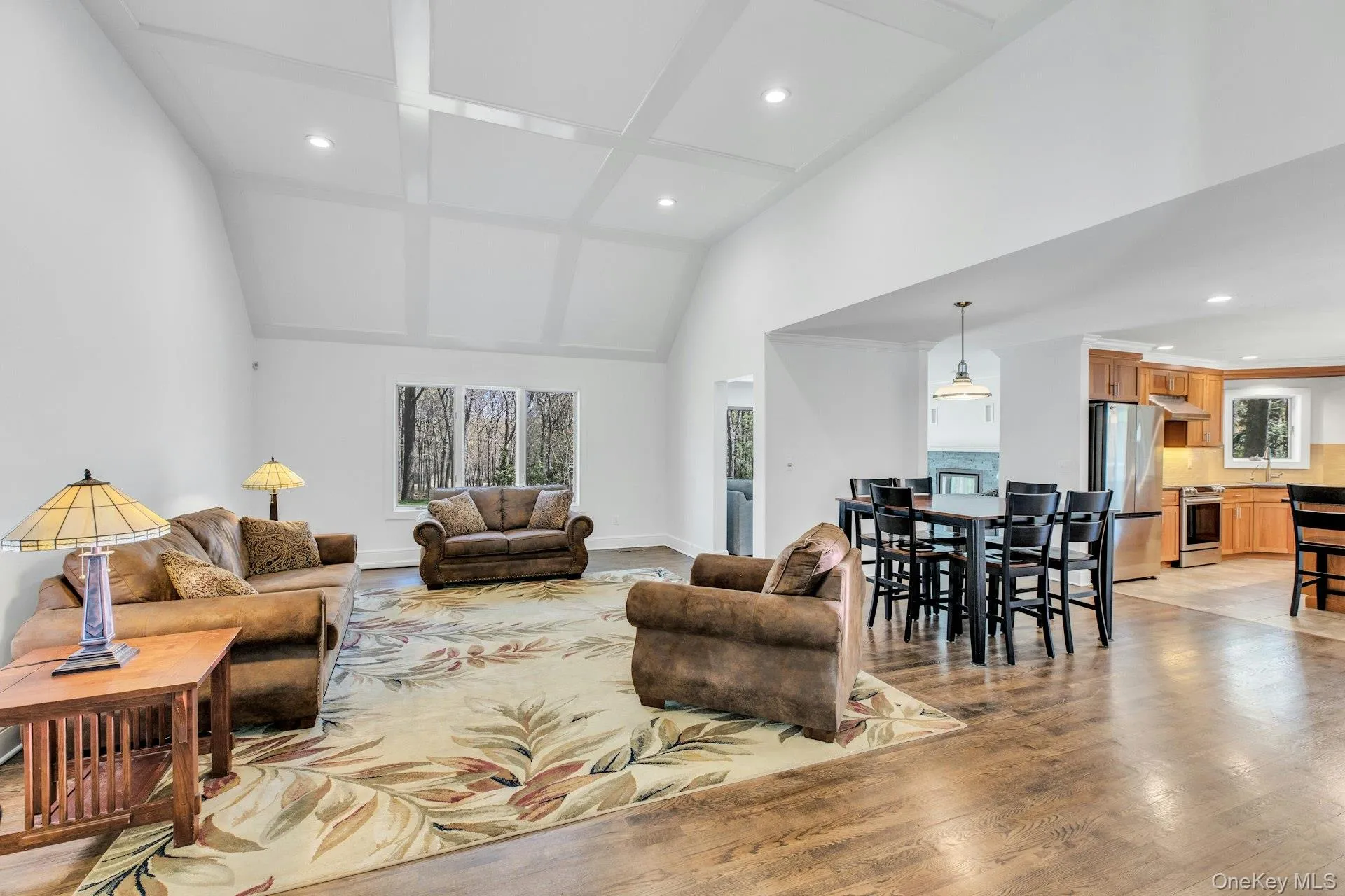 Open-concept living area featuring vaulted ceilings with beam detailing, hardwood flooring, and abundant natural light from multiple windows Open-concept living area featuring vaulted ceilings with beam detailing, hardwood flooring, and abundant natural light from multiple windows
