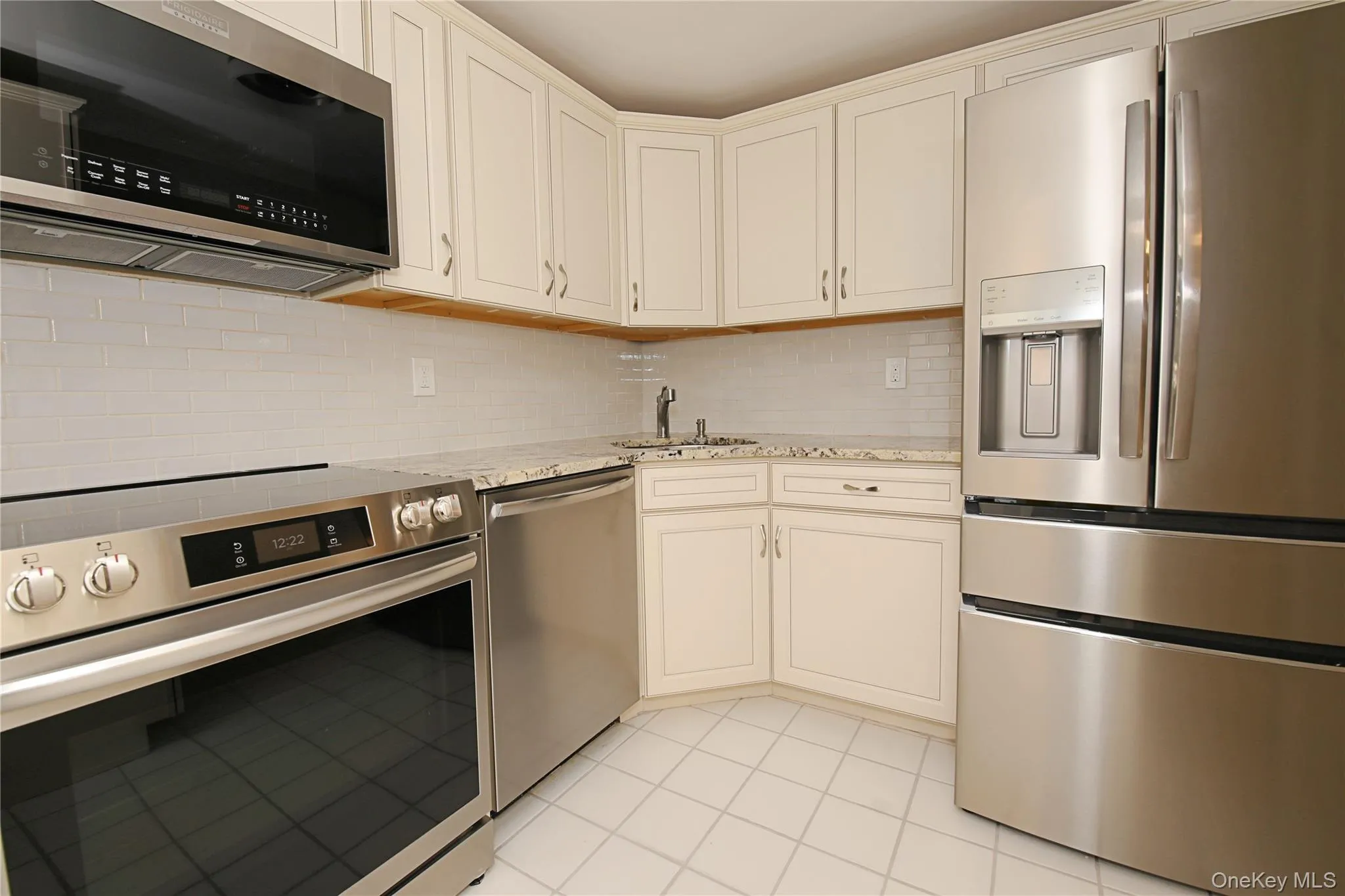 Kitchen featuring white cabinetry, stainless steel appliances, a white tile backsplash, and light-colored countertops Kitchen featuring white cabinetry, stainless steel appliances, a white tile backsplash, and light-colored countertops