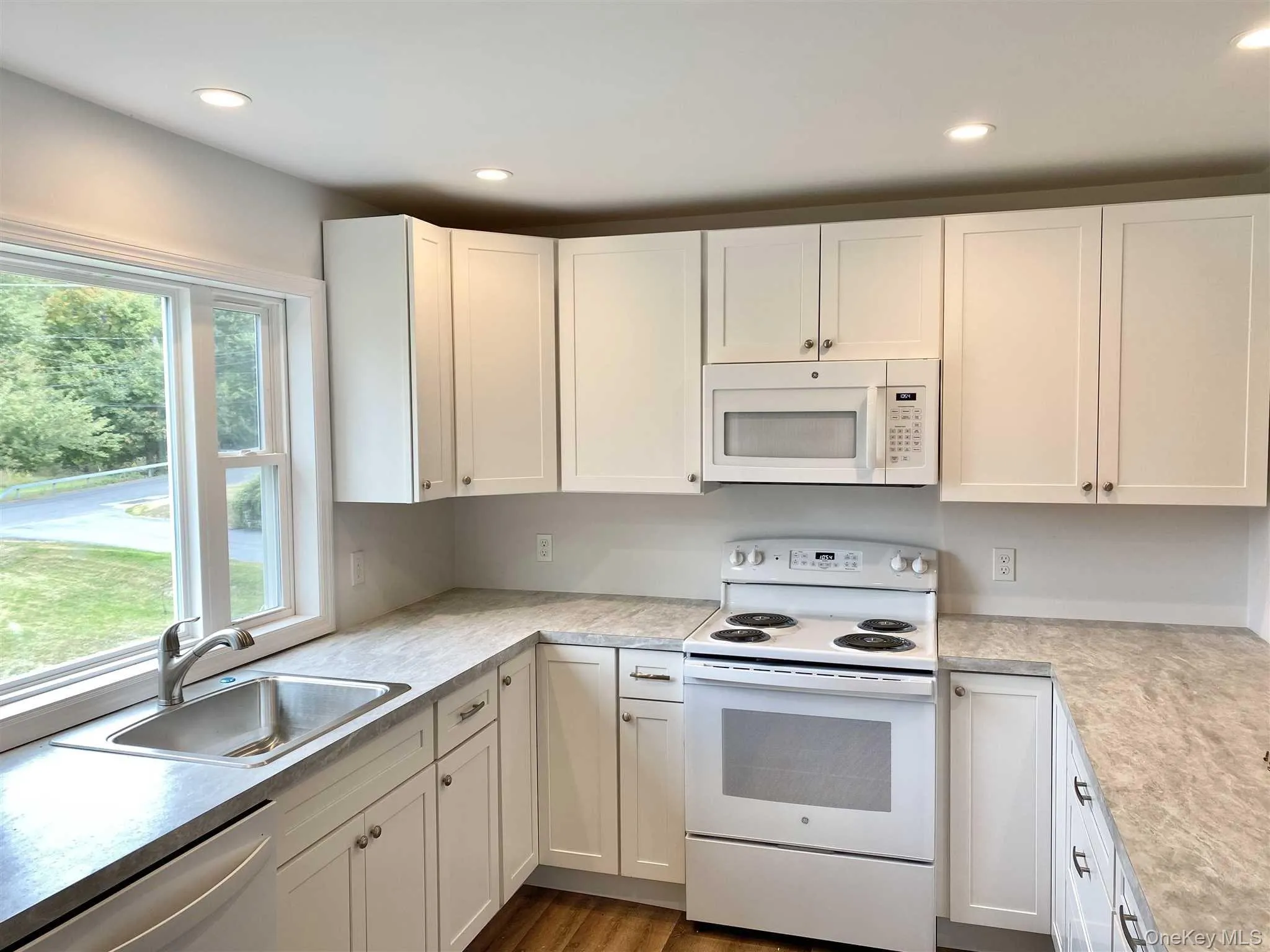 The kitchen features white cabinetry, a stainless steel sink, and white appliances including a stove and microwave and large window The kitchen features white cabinetry, a stainless steel sink, and white appliances including a stove and microwave and large window