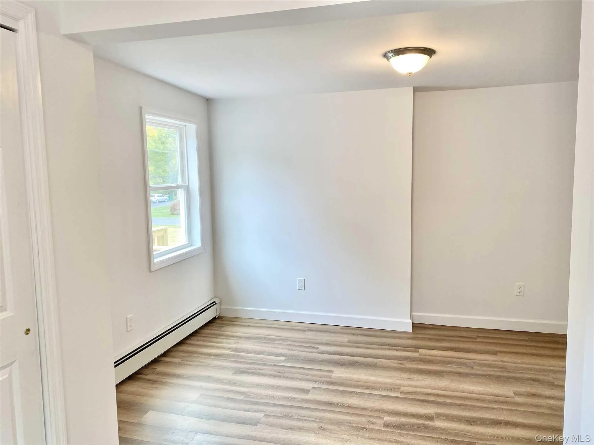 This room features light-toned wood-style flooring, a window providing natural light, and a ceiling-mounted light fixture This room features light-toned wood-style flooring, a window providing natural light, and a ceiling-mounted light fixture