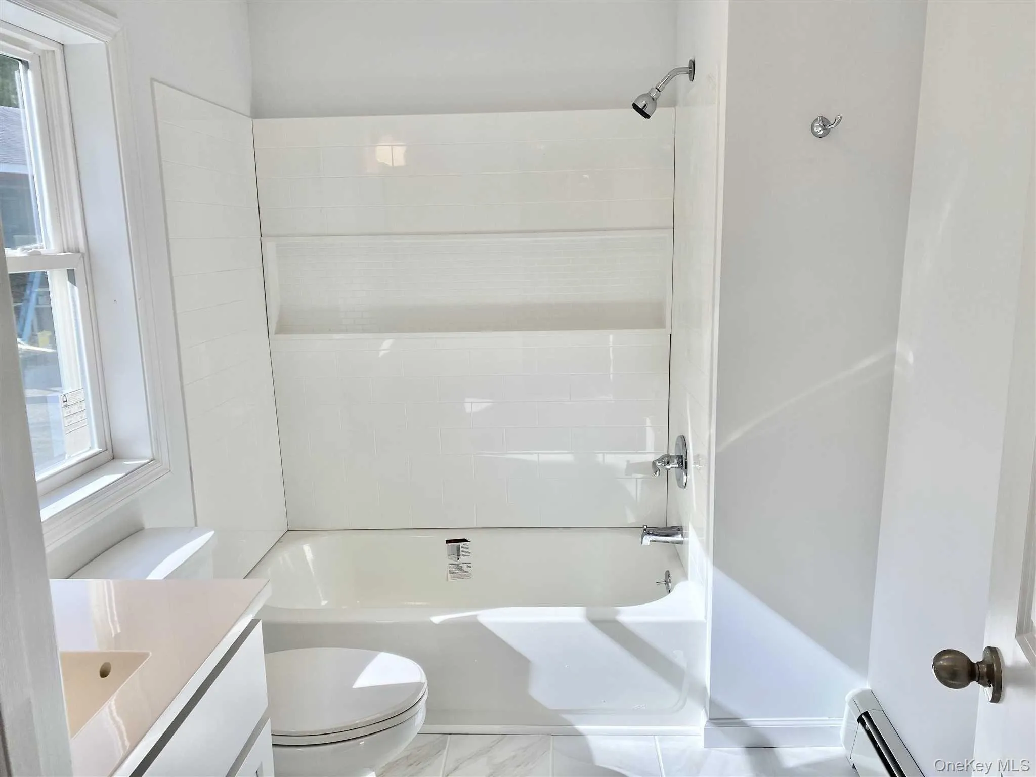 The bathroom features a bathtub with a showerhead, a toilet, a vanity with a sink, and a window providing natural light The bathroom features a bathtub with a showerhead, a toilet, a vanity with a sink, and a window providing natural light
