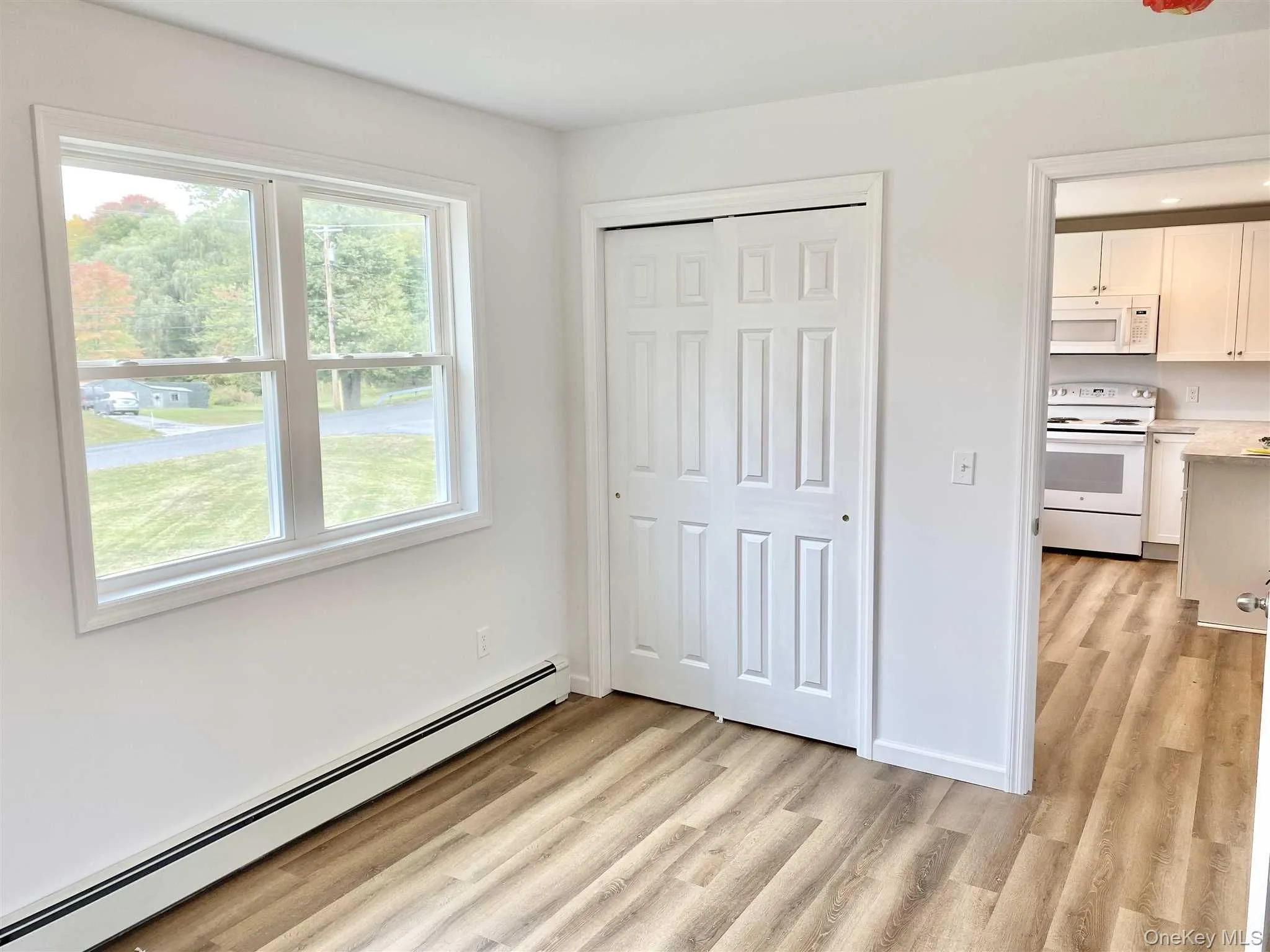 Bright room with a large window, light-toned flooring, and a closet with bifold doors Bright room with a large window, light-toned flooring, and a closet with bifold doors