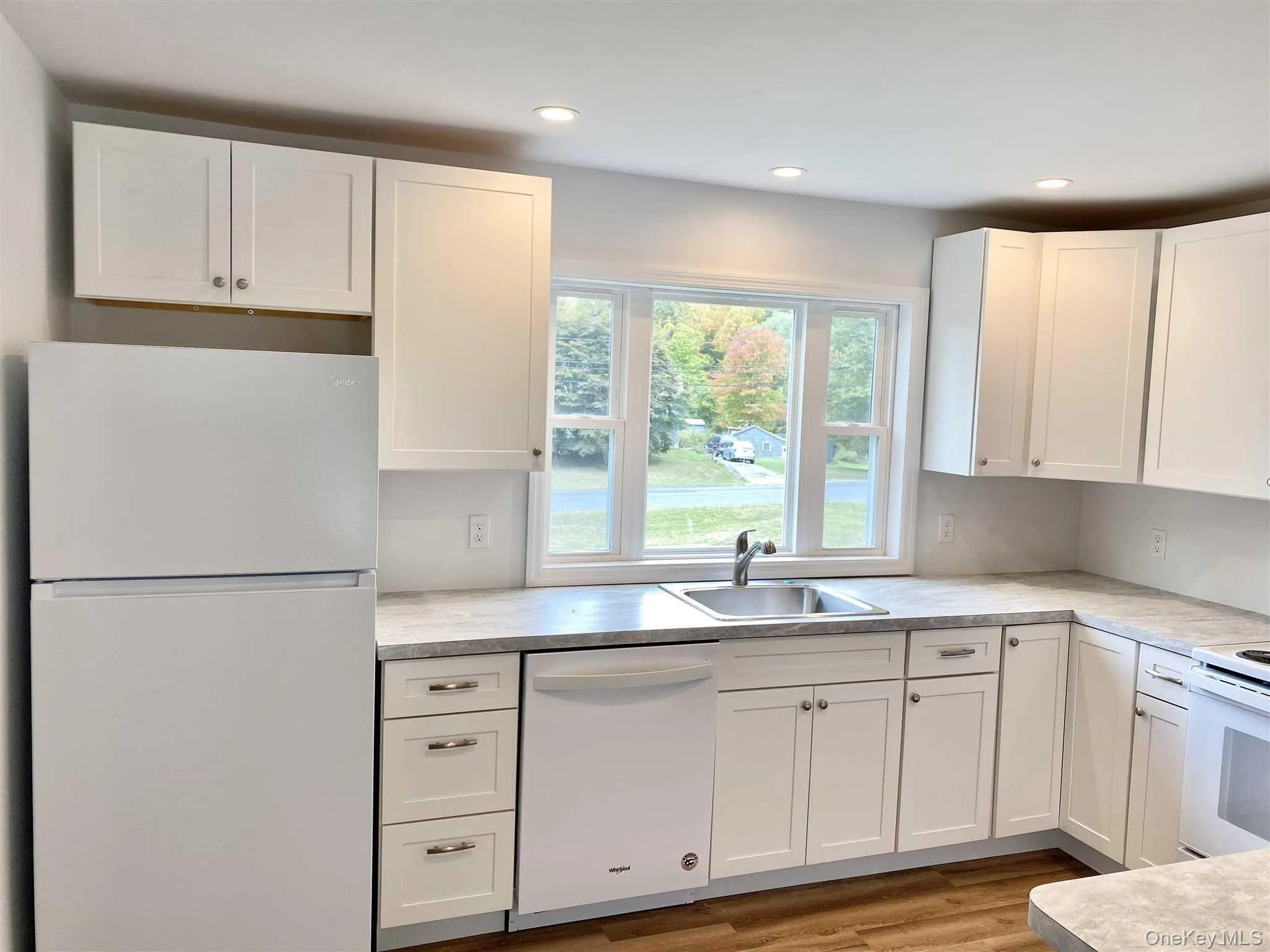 The kitchen features white cabinetry, a stainless steel sink, and white appliances including a refrigerator, dishwasher, and oven The kitchen features white cabinetry, a stainless steel sink, and white appliances including a refrigerator, dishwasher, and oven