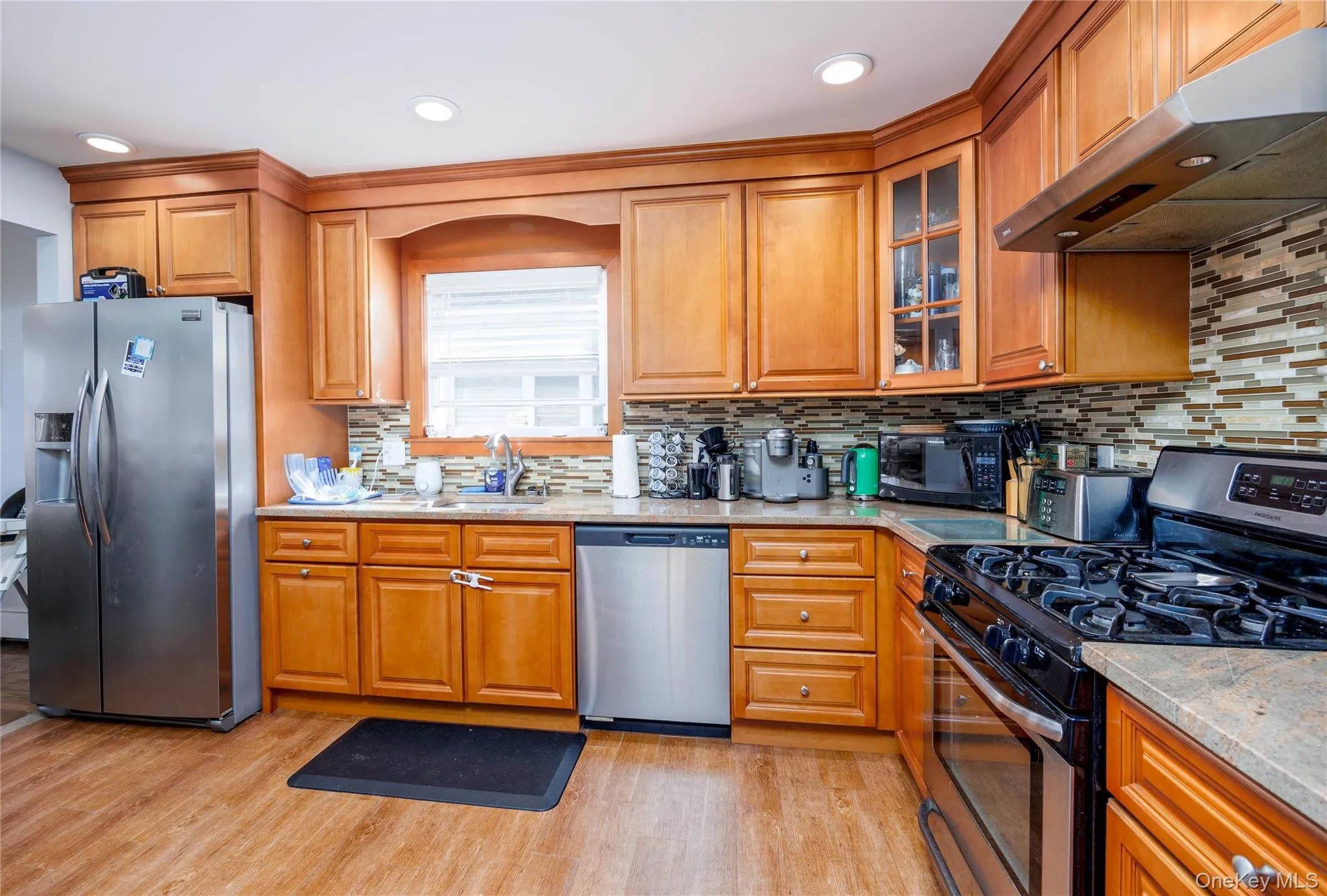 Kitchen featuring stainless steel appliances, under cabinet range hood, brown cabinets, light wood finished floors, and recessed lighting Kitchen featuring stainless steel appliances, under cabinet range hood, brown cabinets, light wood finished floors, and recessed lighting