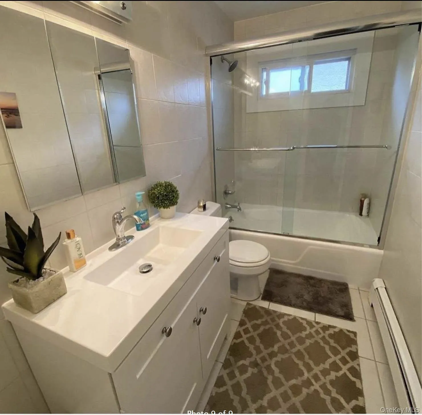 Full bath with a baseboard heating unit, tile walls, toilet, vanity, and tile patterned flooring Full bath with a baseboard heating unit, tile walls, toilet, vanity, and tile patterned flooring