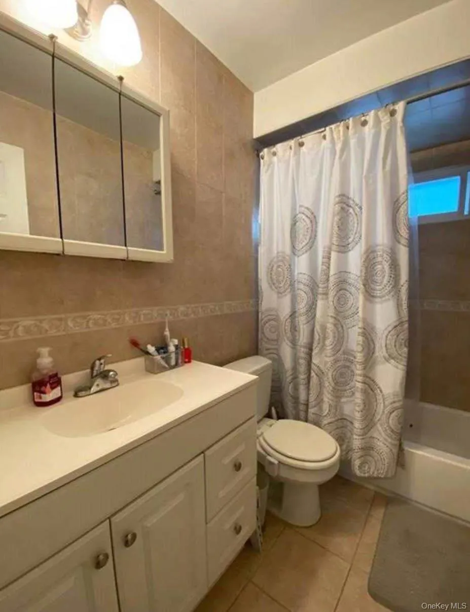 Full bathroom featuring tile walls, tile patterned floors, vanity, shower / tub combo with curtain, and toilet Full bathroom featuring tile walls, tile patterned floors, vanity, shower / tub combo with curtain, and toilet