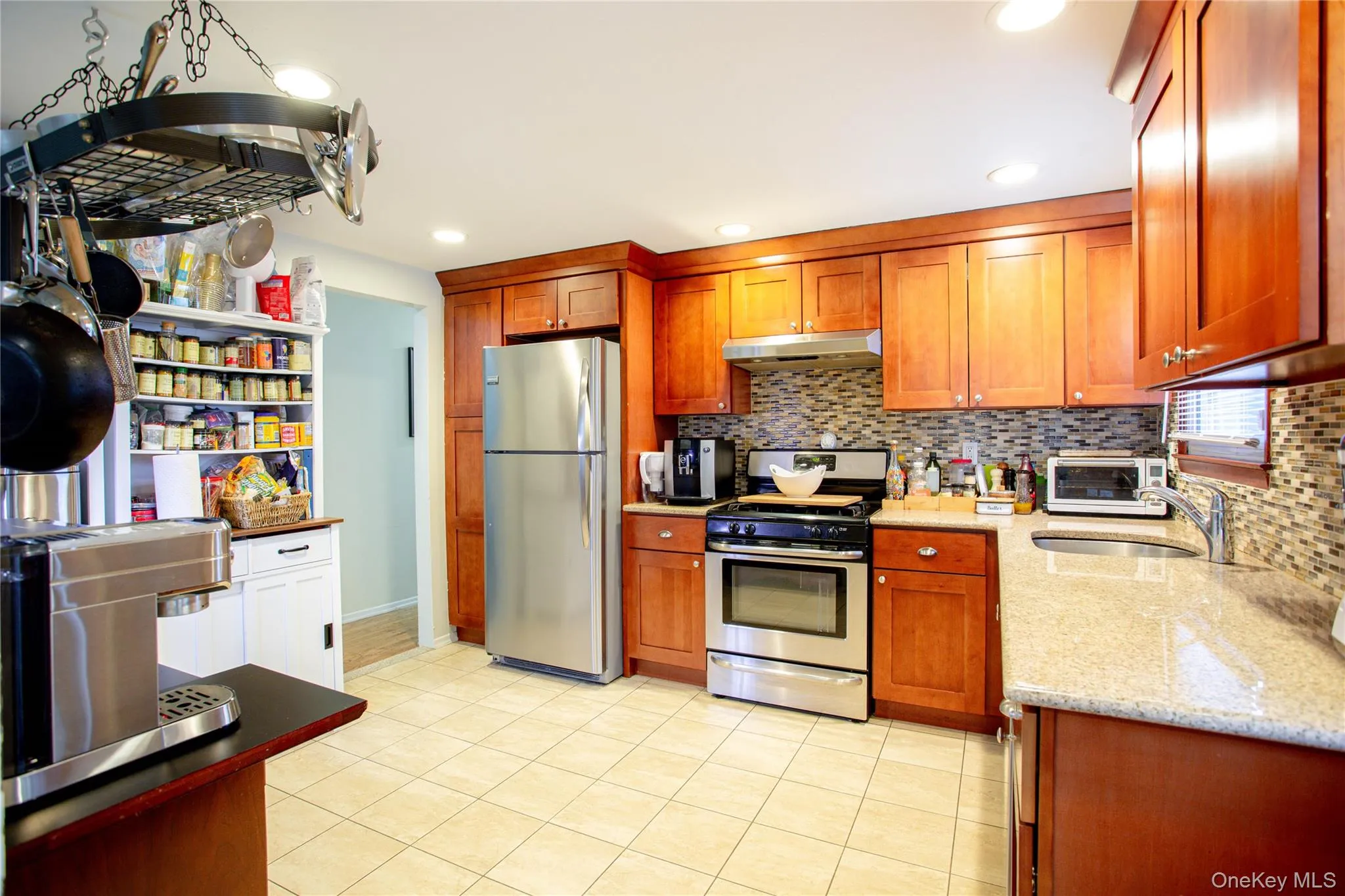 Kitchen featuring decorative backsplash, under cabinet range hood, light stone countertops, and appliances with stainless steel finishes Kitchen featuring decorative backsplash, under cabinet range hood, light stone countertops, and appliances with stainless steel finishes