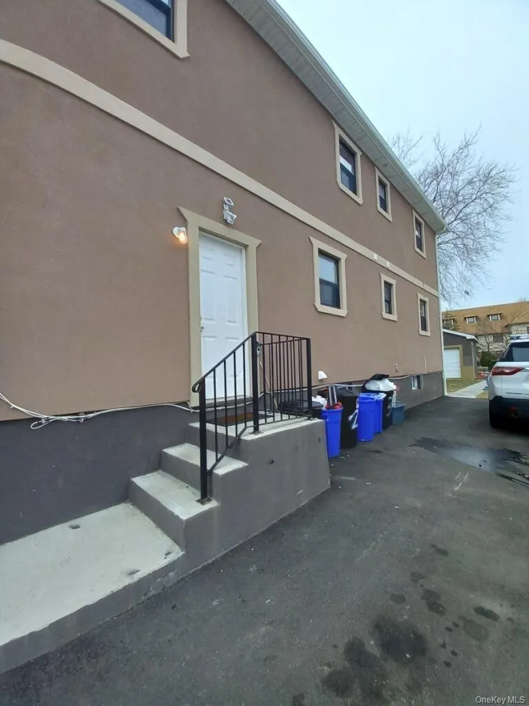 The property features a stucco exterior with decorative trim around the windows and entryway, a private entrance with concrete steps and a black metal handrail, and a paved driveway The property features a stucco exterior with decorative trim around the windows and entryway, a private entrance with concrete steps and a black metal handrail, and a paved driveway