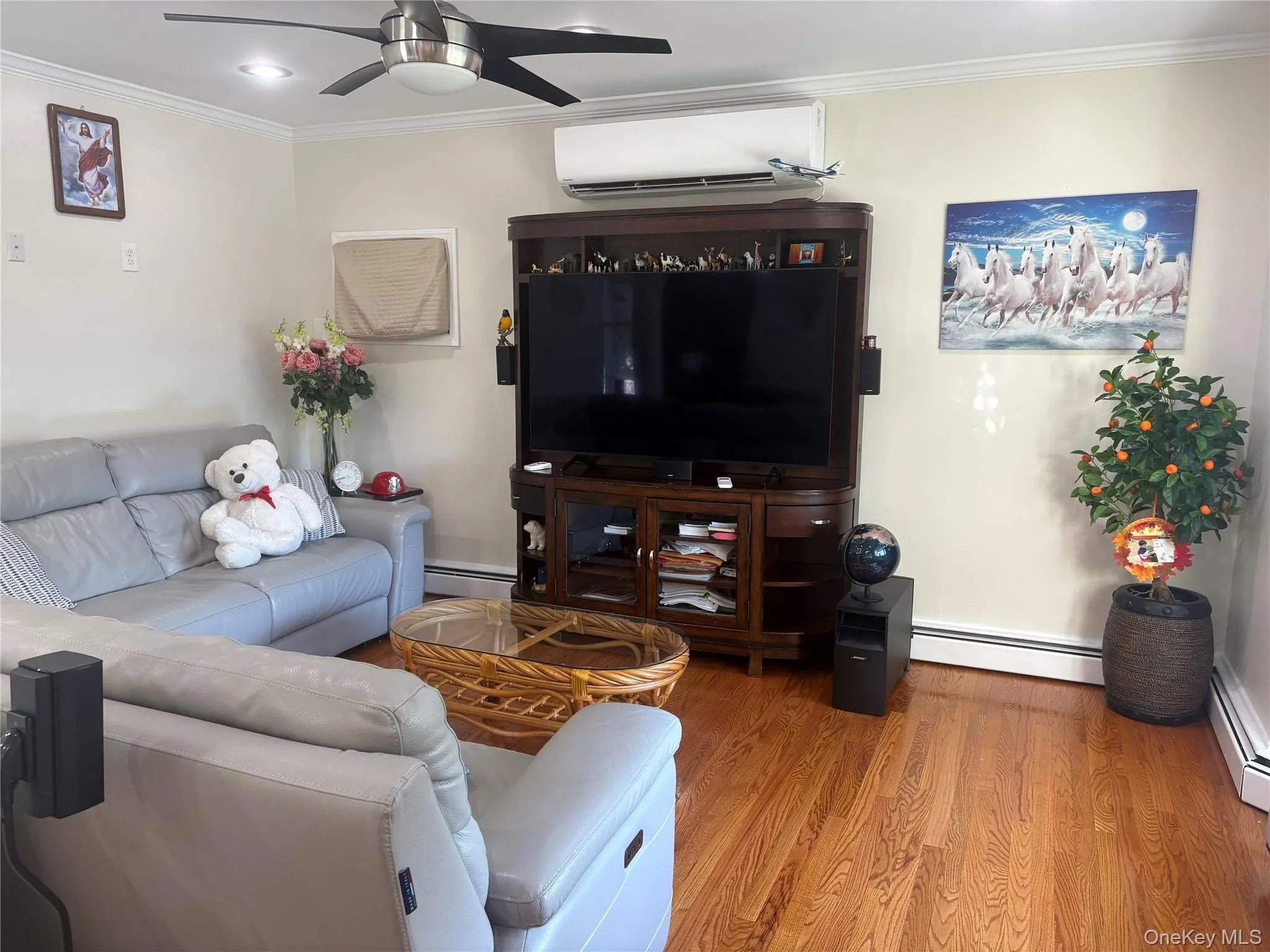 Living area featuring wood-finish flooring, recessed lighting, crown molding, a ceiling fan with integrated lighting, and a wall-mounted mini-split system Living area featuring wood-finish flooring, recessed lighting, crown molding, a ceiling fan with integrated lighting, and a wall-mounted mini-split system