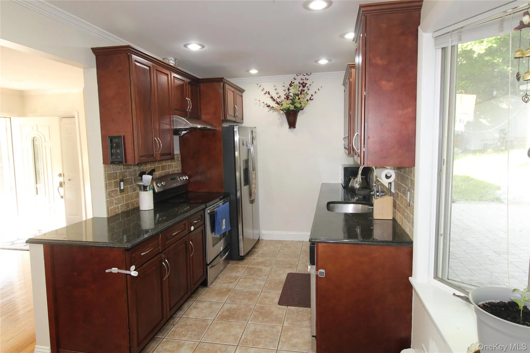 Galley kitchen featuring rich wood cabinetry, dark countertops, tiled flooring, stainless steel appliances, and recessed lighting Galley kitchen featuring rich wood cabinetry, dark countertops, tiled flooring, stainless steel appliances, and recessed lighting