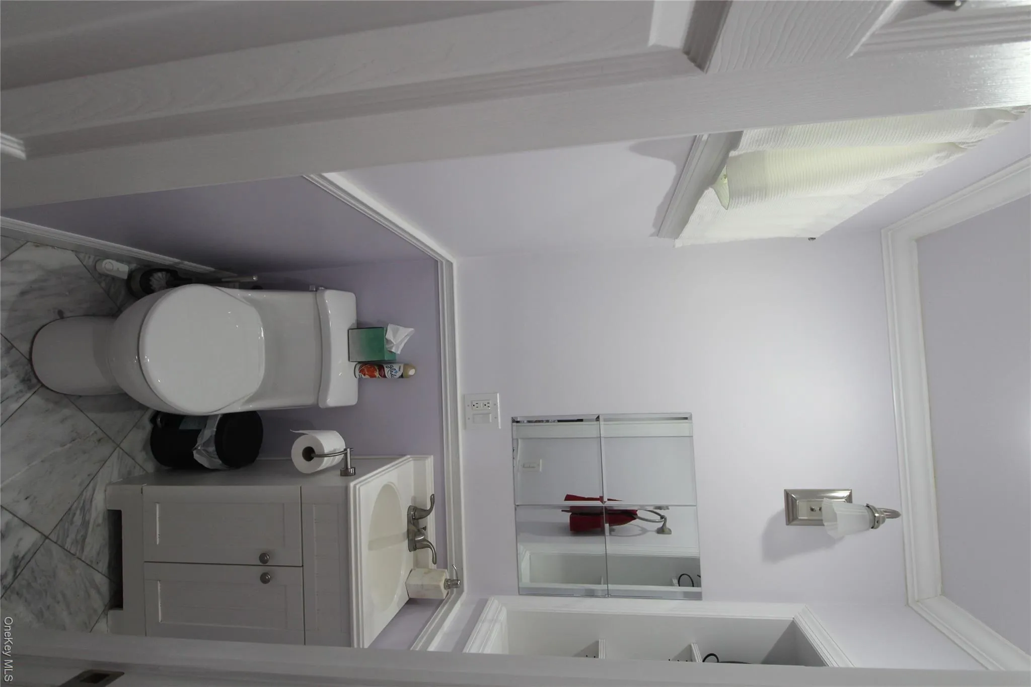 Compact powder room featuring a single-piece toilet, a white vanity with an integrated sink, wall-mounted sconce lighting, and crown molding is located in 1st Bedroom. Compact powder room featuring a single-piece toilet, a white vanity with an integrated sink, wall-mounted sconce lighting, and crown molding is located in 1st Bedroom.