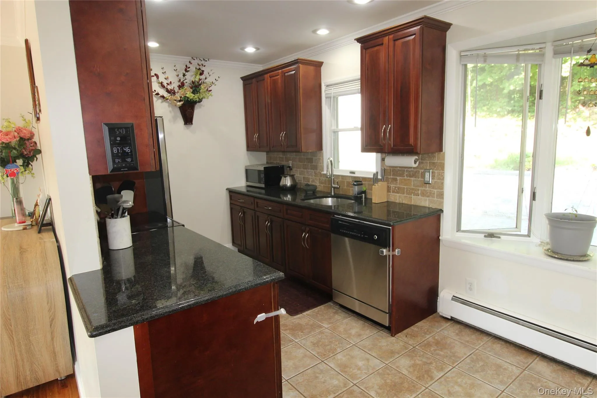 Kitchen featuring dark wood cabinetry, stainless steel dishwasher, speckled black countertops, and a tiled backsplash. Walk out to screened in porch and backyard. Kitchen featuring dark wood cabinetry, stainless steel dishwasher, speckled black countertops, and a tiled backsplash. Walk out to screened in porch and backyard.