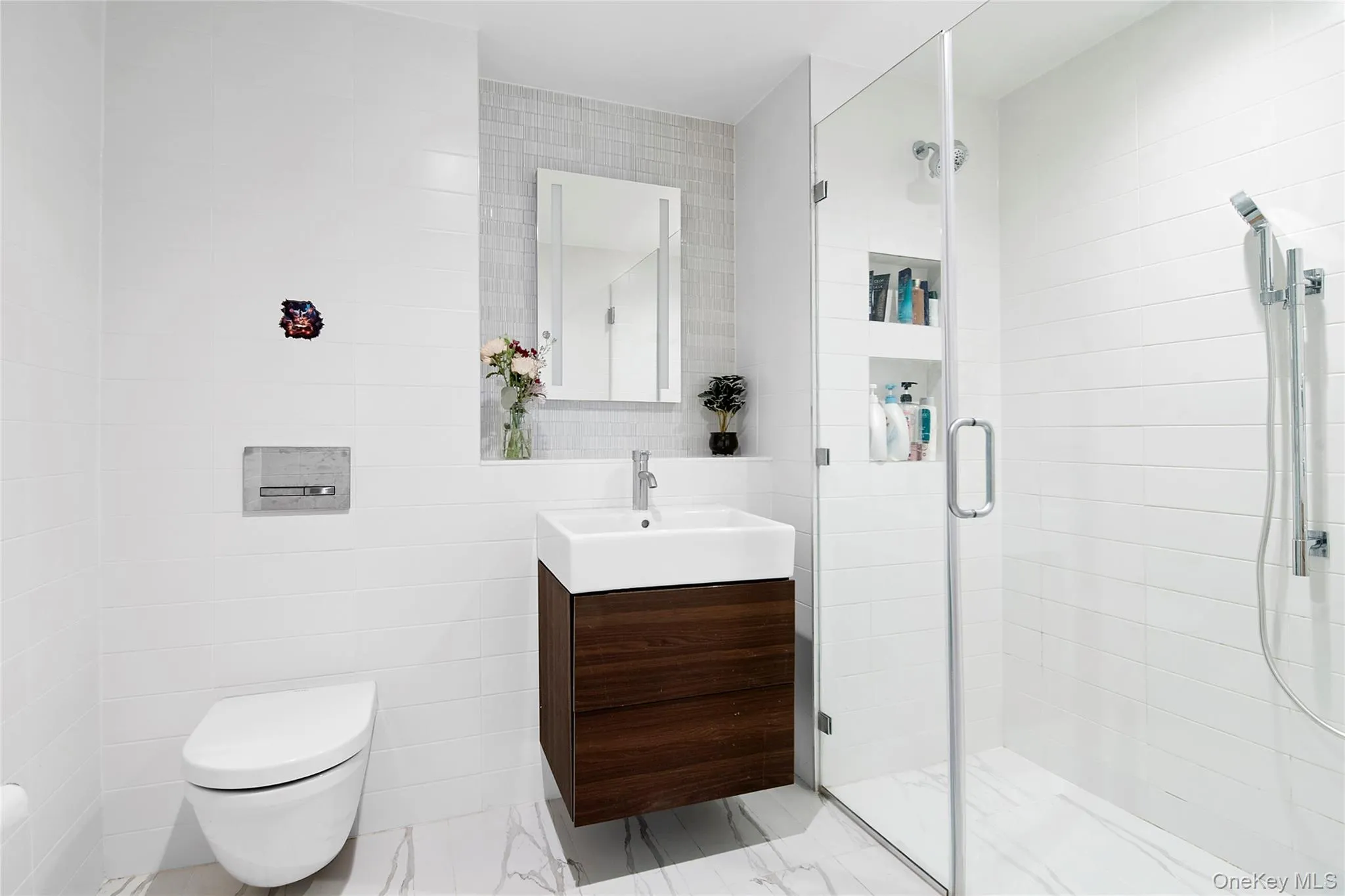 Contemporary bathroom featuring heated floors, a floating wood-finish vanity with a vessel sink, a mirrored medicine cabinet, a frameless glass shower enclosure with built-in shelving, a wall-mounted toilet, and large format tile flooring Contemporary bathroom featuring heated floors, a floating wood-finish vanity with a vessel sink, a mirrored medicine cabinet, a frameless glass shower enclosure with built-in shelving, a wall-mounted toilet, and large format tile flooring