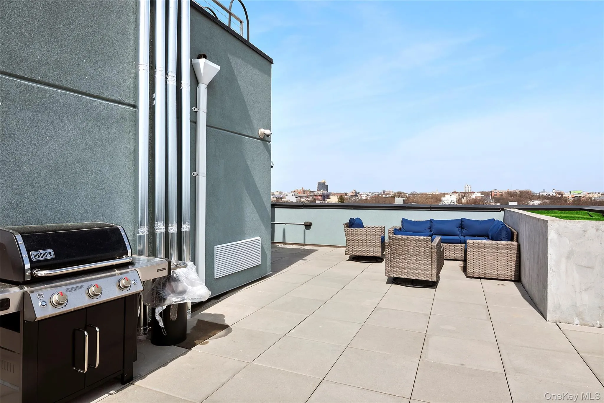 Expansive rooftop terrace featuring large format paver flooring, a perimeter wall with artificial turf accent, a flat roofline, and a cityscape horizon Expansive rooftop terrace featuring large format paver flooring, a perimeter wall with artificial turf accent, a flat roofline, and a cityscape horizon