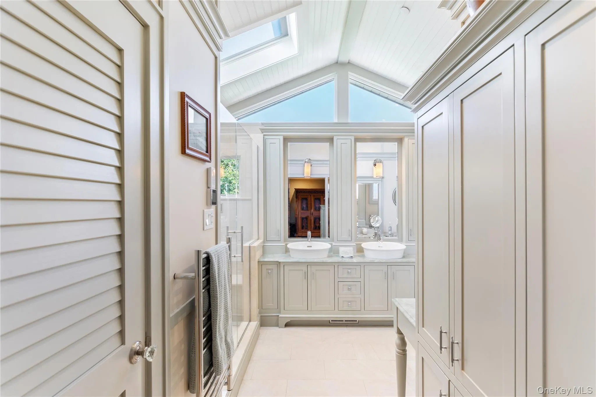 Full bathroom featuring lofted ceiling with skylight, dual vanity sink, custom cabinetry and trim work, and radiant heat floors Full bathroom featuring lofted ceiling with skylight, dual vanity sink, custom cabinetry and trim work, and radiant heat floors