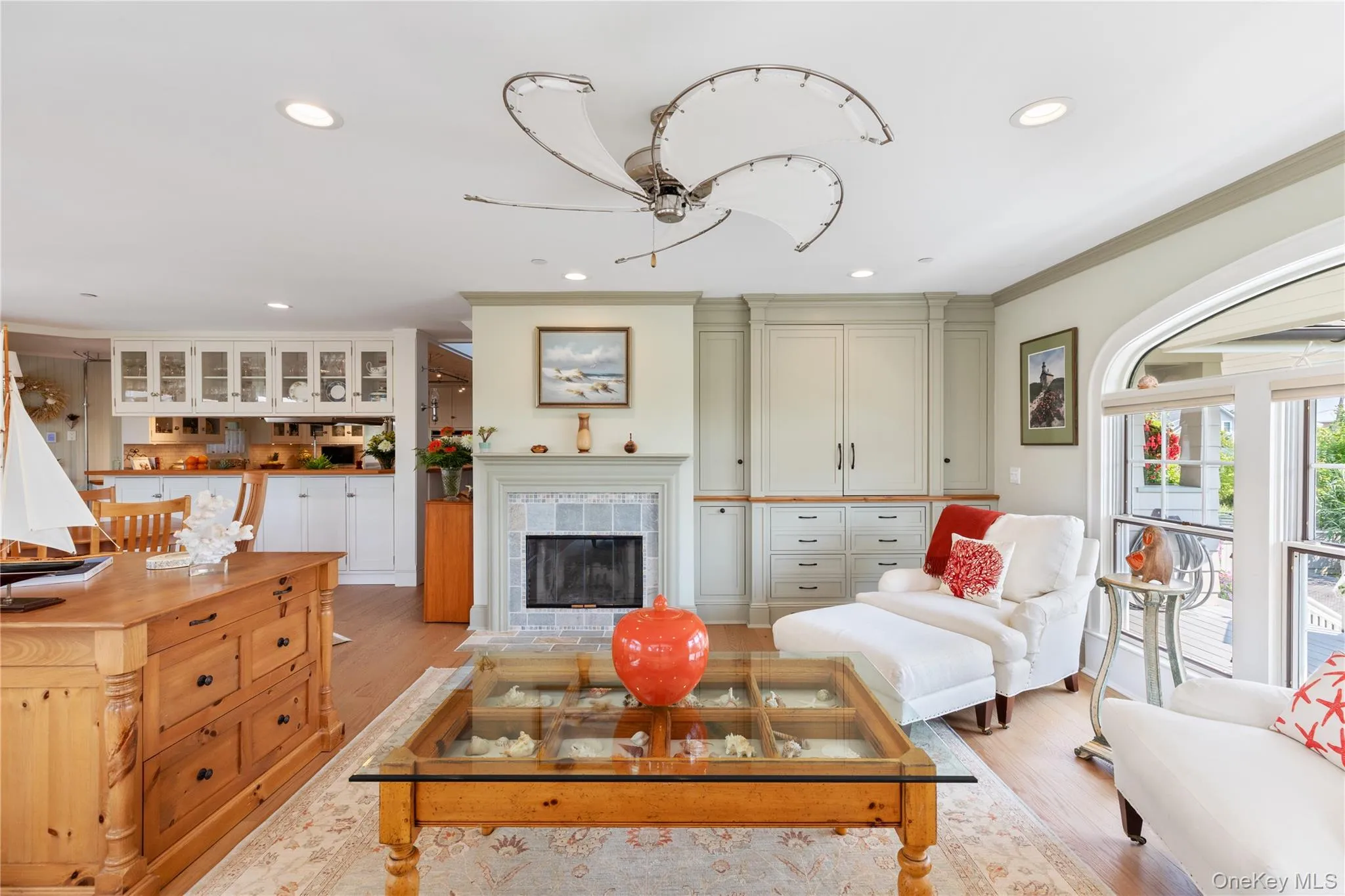Living room with light wood-type flooring, crown molding, built in cabinets with television inside, and a tiled wood burning fireplace Living room with light wood-type flooring, crown molding, built in cabinets with television inside, and a tiled wood burning fireplace