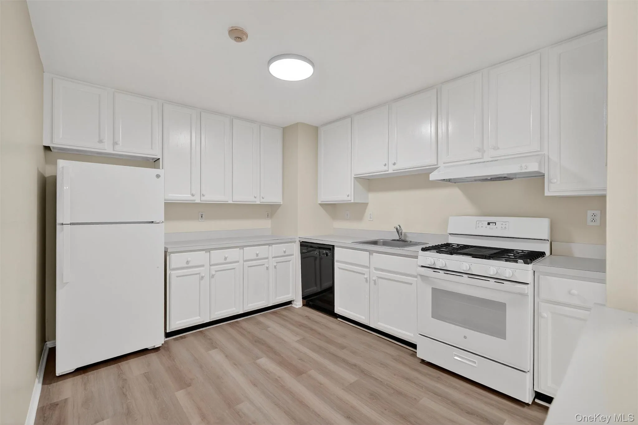 Kitchen featuring white appliances, light countertops, light wood finished floors, under cabinet range hood, and white cabinetry Kitchen featuring white appliances, light countertops, light wood finished floors, under cabinet range hood, and white cabinetry