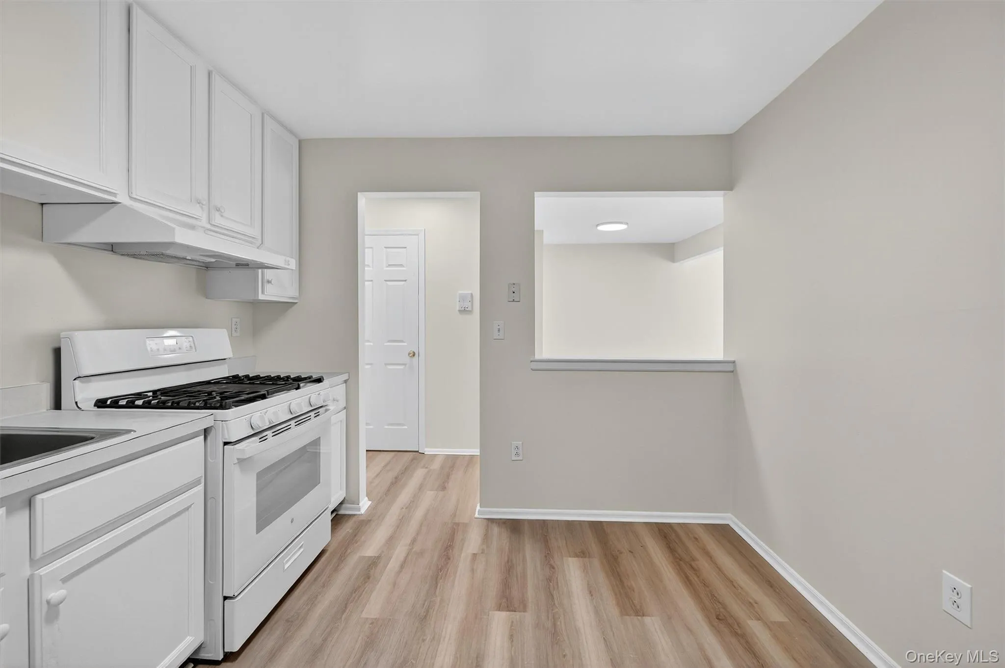 Kitchen with white range with gas stovetop, white cabinets, light countertops, and light wood-style flooring Kitchen with white range with gas stovetop, white cabinets, light countertops, and light wood-style flooring