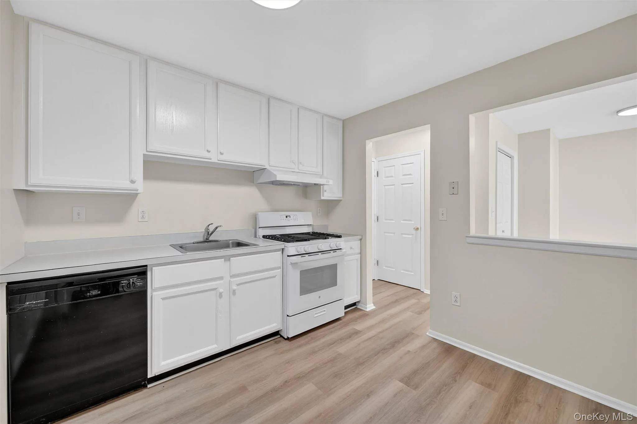 Kitchen with dishwasher, white range with gas stovetop, white cabinetry, light wood finished floors, and light countertops Kitchen with dishwasher, white range with gas stovetop, white cabinetry, light wood finished floors, and light countertops