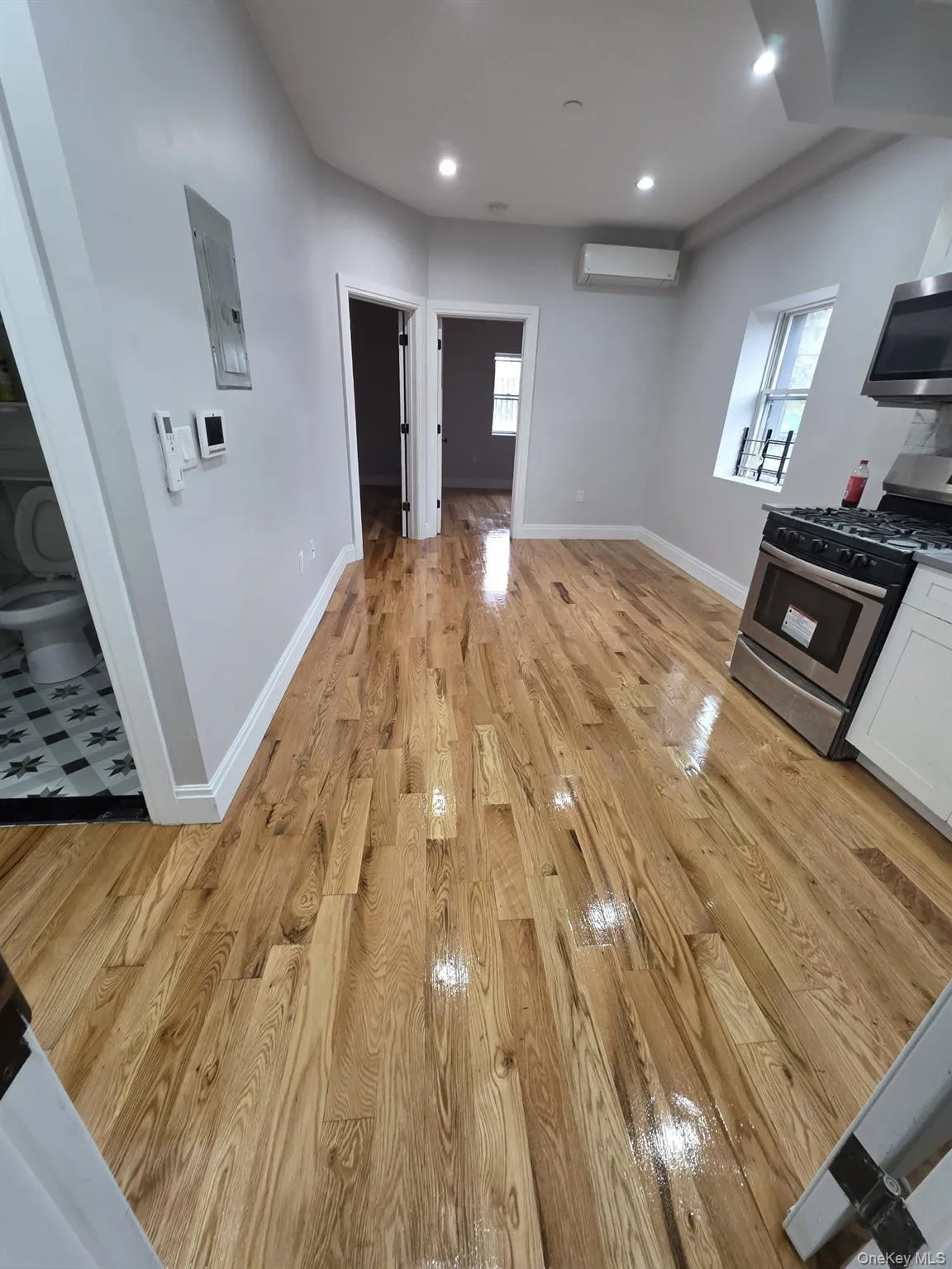 Open-concept living space featuring wood-finish flooring, recessed lighting, and a kitchen area with stainless steel appliances Open-concept living space featuring wood-finish flooring, recessed lighting, and a kitchen area with stainless steel appliances