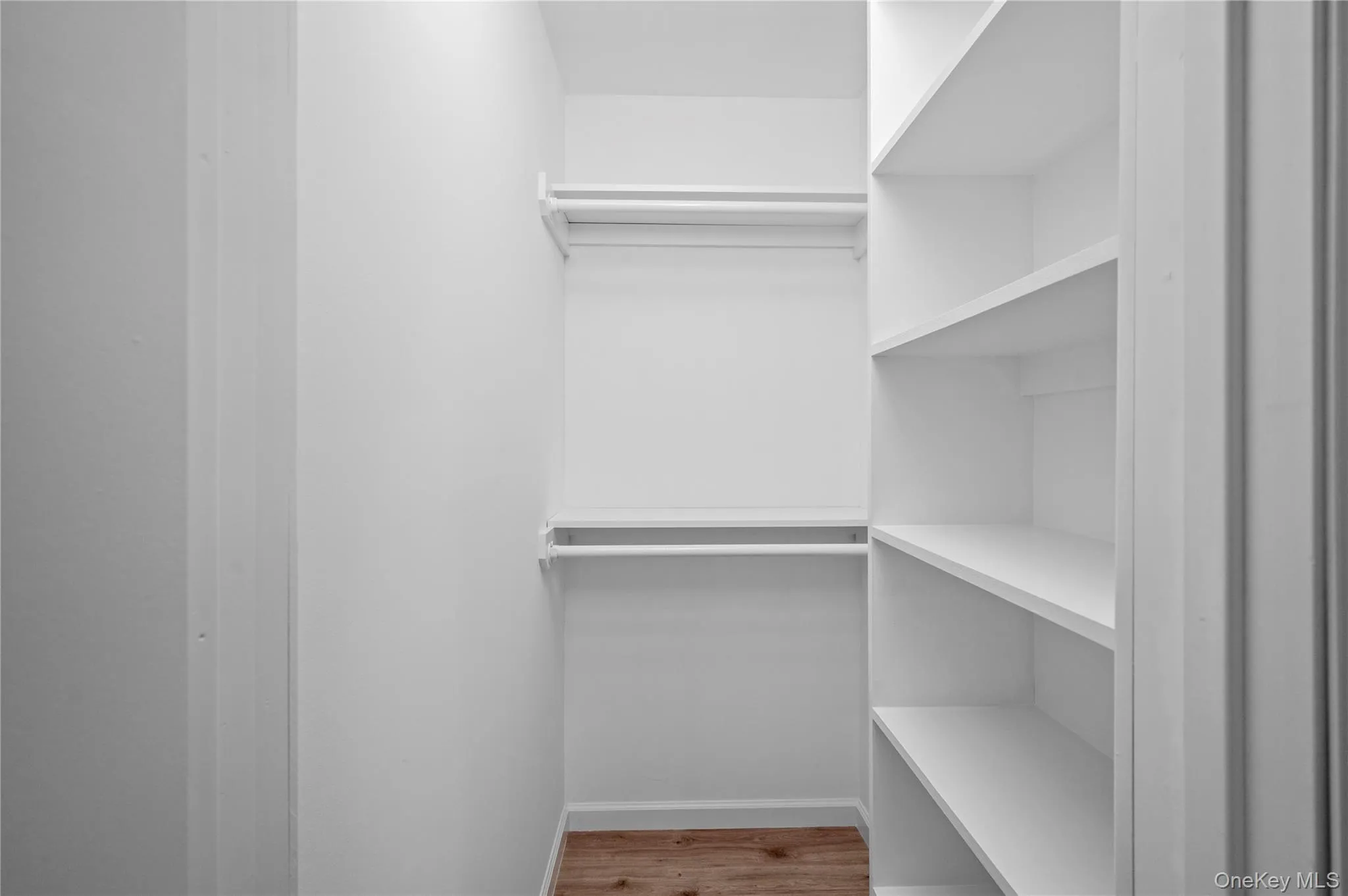 This closet features built-in white shelving, two clothing rods, and wood-style flooring This closet features built-in white shelving, two clothing rods, and wood-style flooring