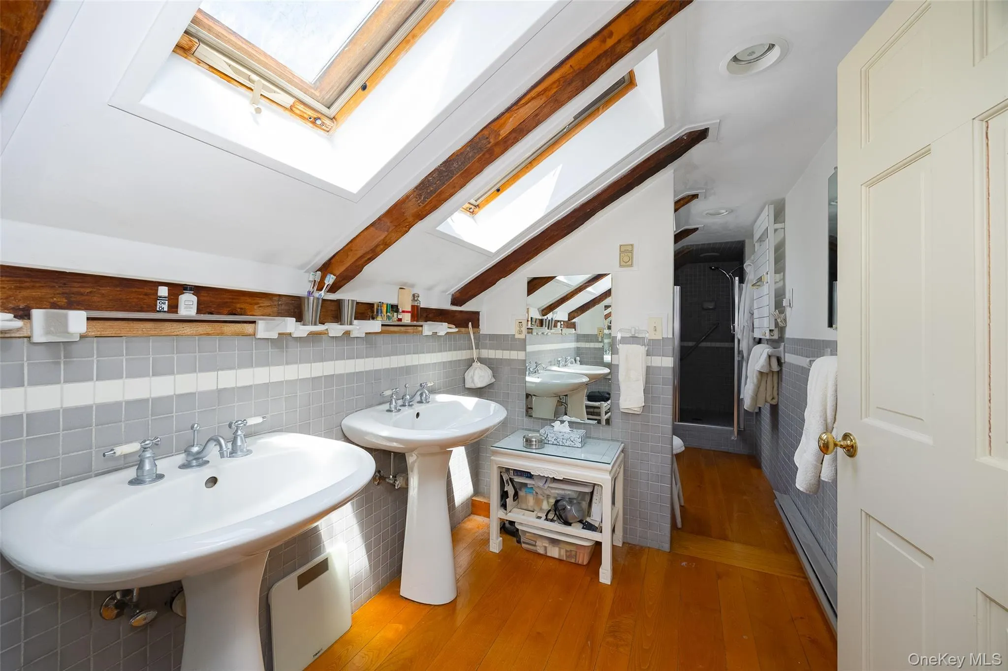 Bathroom featuring dual pedestal sinks, wood flooring, and exposed hand-hewn beams and skylights Bathroom featuring dual pedestal sinks, wood flooring, and exposed hand-hewn beams and skylights