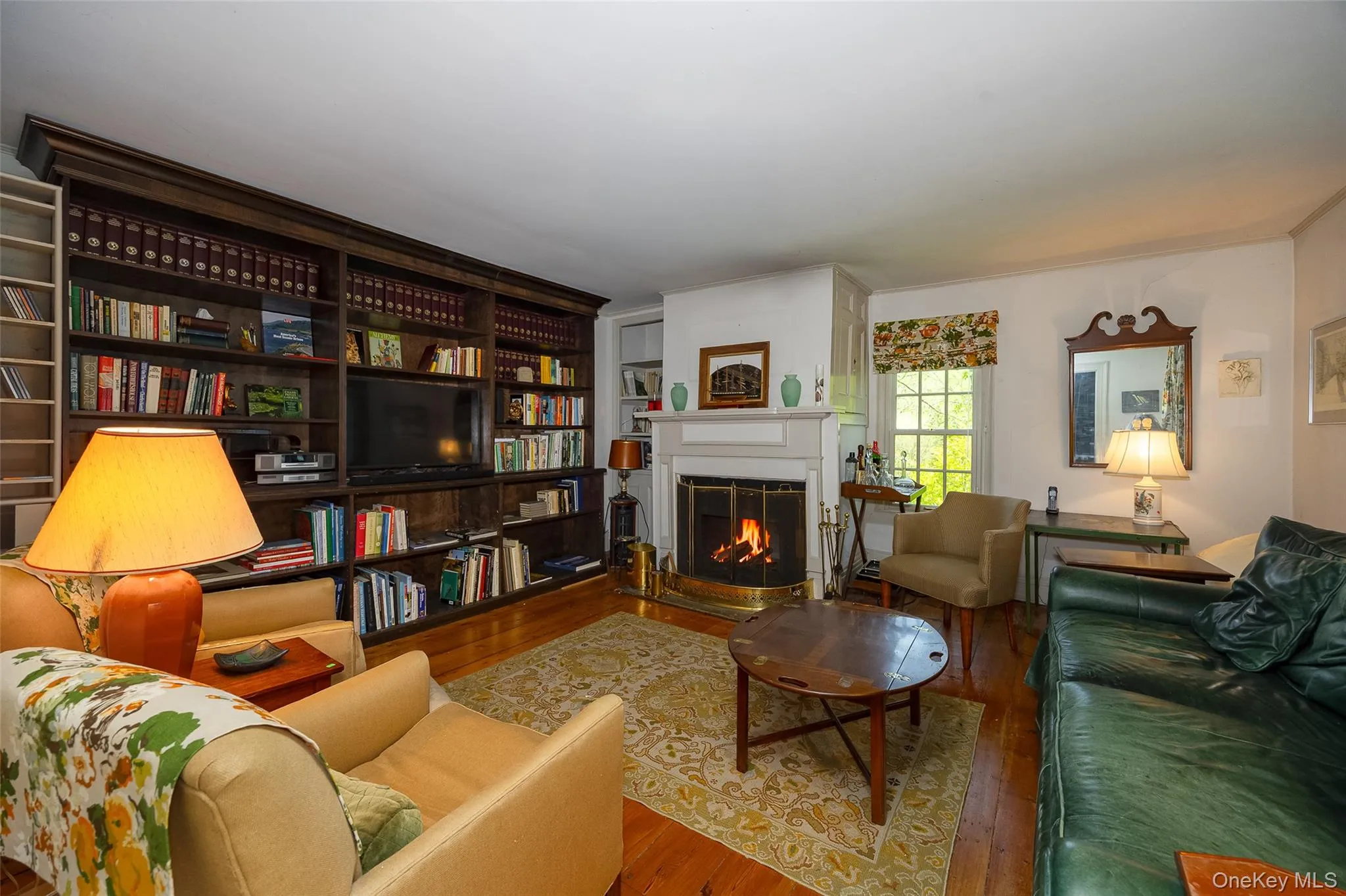 Living area featuring rich wood-finish flooring and a central fireplace with a white mantel Living area featuring rich wood-finish flooring and a central fireplace with a white mantel