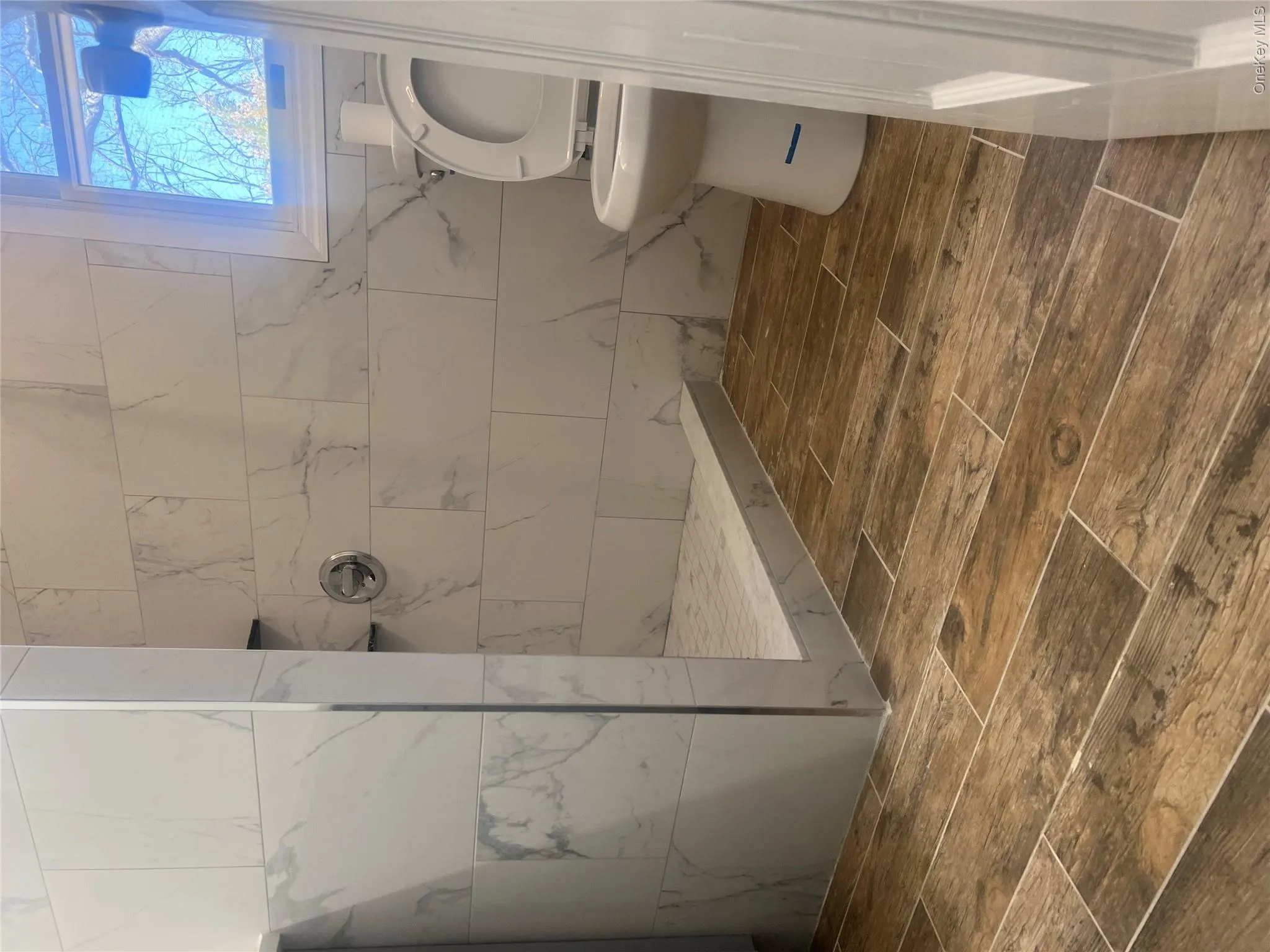 Bathroom featuring wood-look tile flooring and a walk-in shower with white marble-style tile walls Bathroom featuring wood-look tile flooring and a walk-in shower with white marble-style tile walls