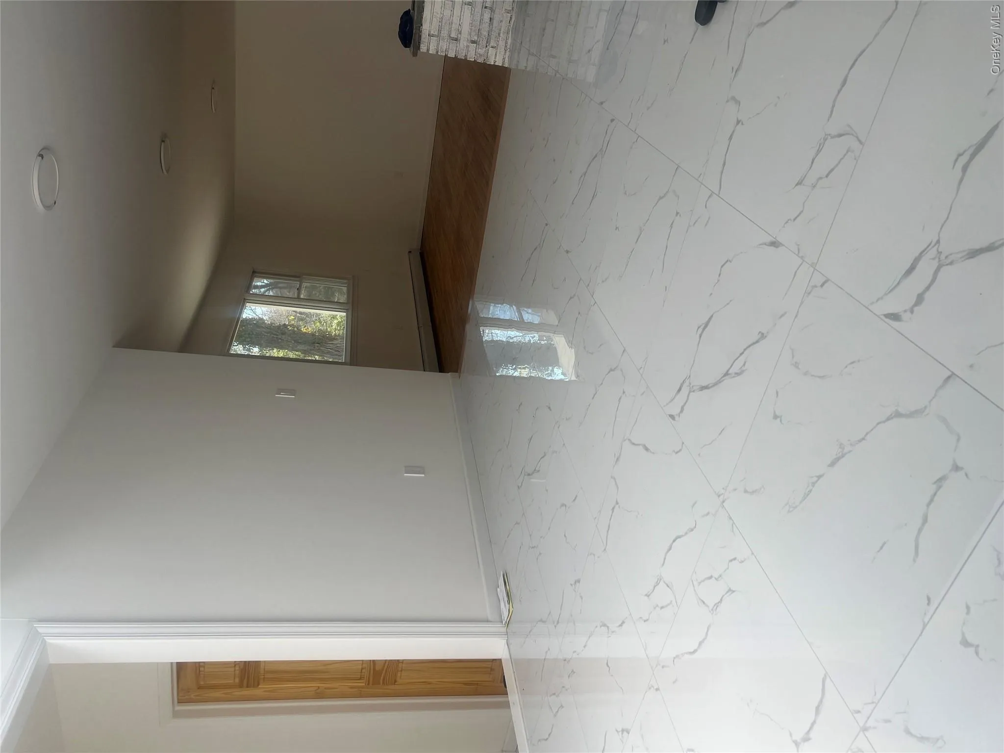 This interior space features white walls and gleaming large format white tiles with grey veining This interior space features white walls and gleaming large format white tiles with grey veining